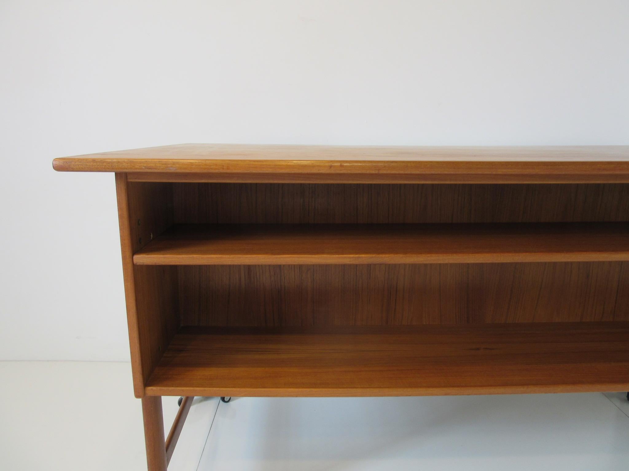 A well crafted teak wood desk with a built in bookcase to the backside having a adjustable shelve, to the front there's three drawers with a upper pullout writing surface, the other side has a file drawer all with teak handles. Designed in the