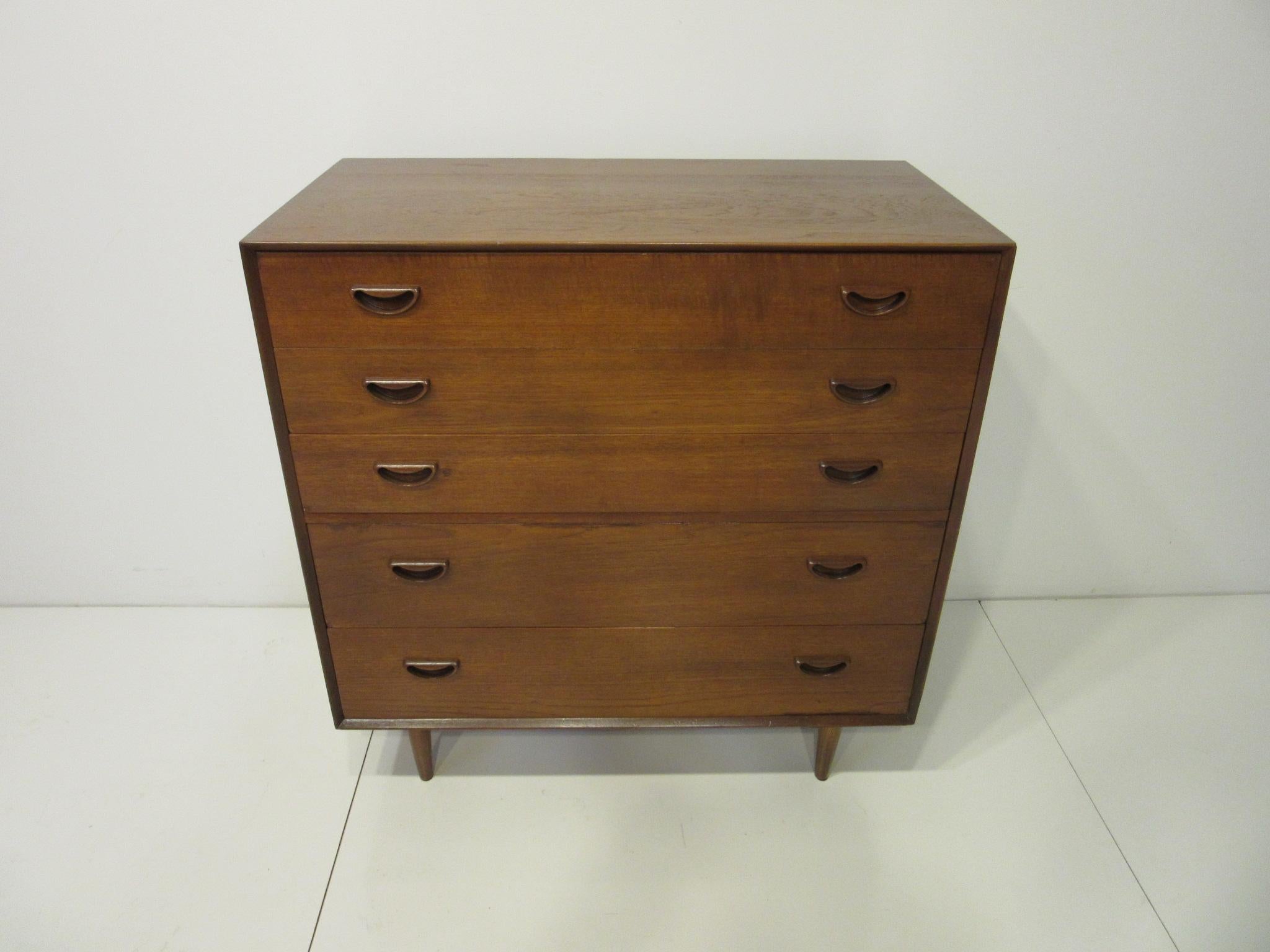 A five-drawer dresser / chest in teak wood with sculptural cut-out pulls with the top edges having dove tail finger joint construction. The two upper drawers have built in dividers and the lower drawers have plenty of storage. Retains the