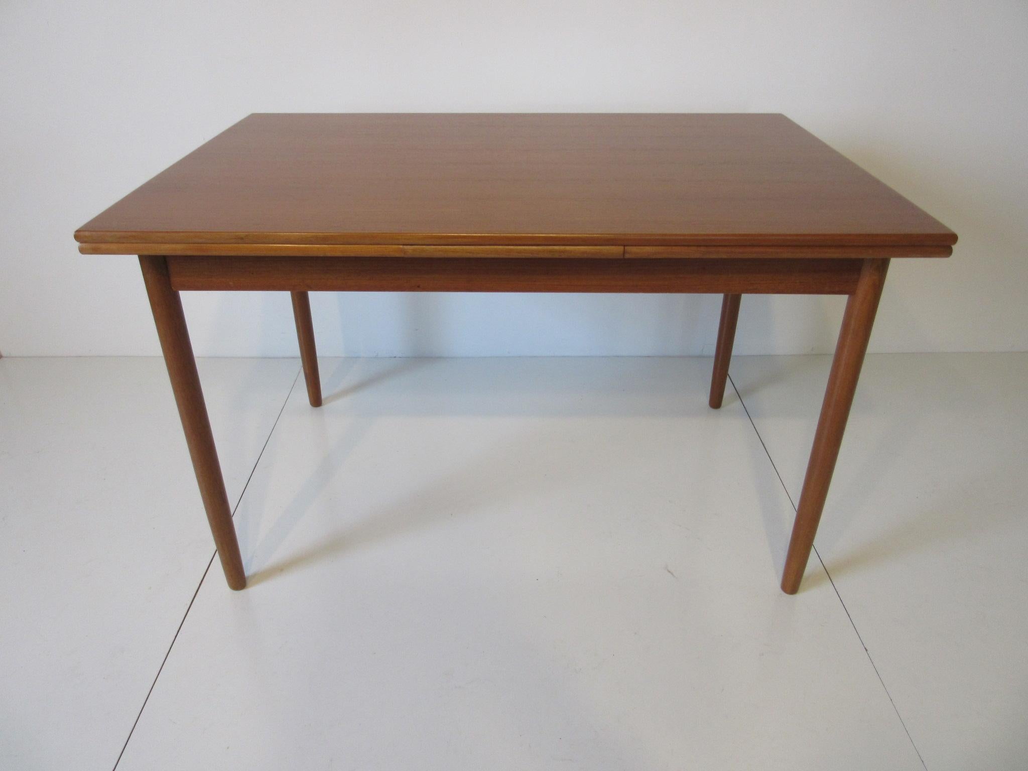 A teak wood extension table with pullout / pull-out leaves to each end and having a finely grained wood surface standing on conical legs, made in Denmark by L & F Mobler. The measurement of the leaves are 17.75