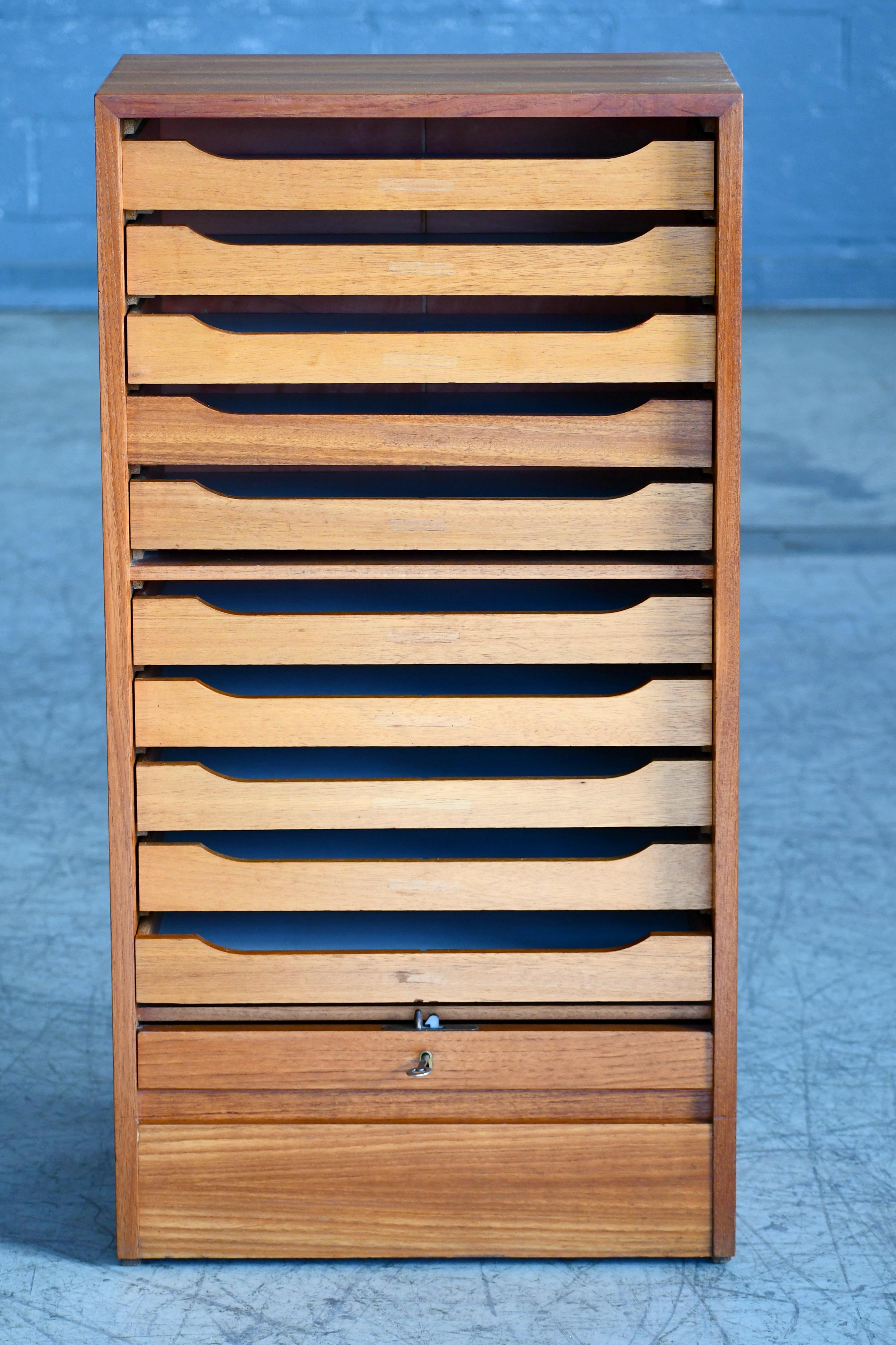 Handsome and versatile high-quality file cabinet in teak made in Denmark in the 1950s. The front has a pull-up tambour door that is lockable with key. Great color and grain and just minor natural age wear including a few minor nicks to the back