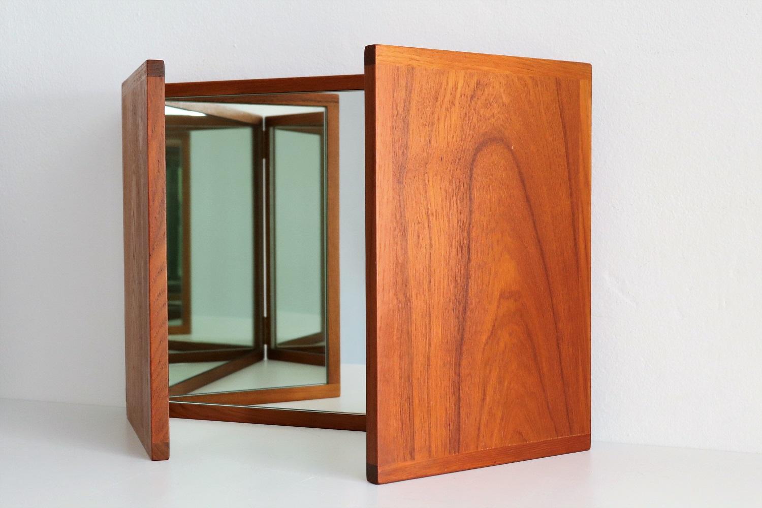 Folding triptych wall-mounted or alternatively tabletop mirror crafted in beautiful teak wood.
Designed by Kai Kristiansen for company Aksel Kjersgaard during the 1960s, Denmark.
The mirror is composed of three hinged-sections (the two end