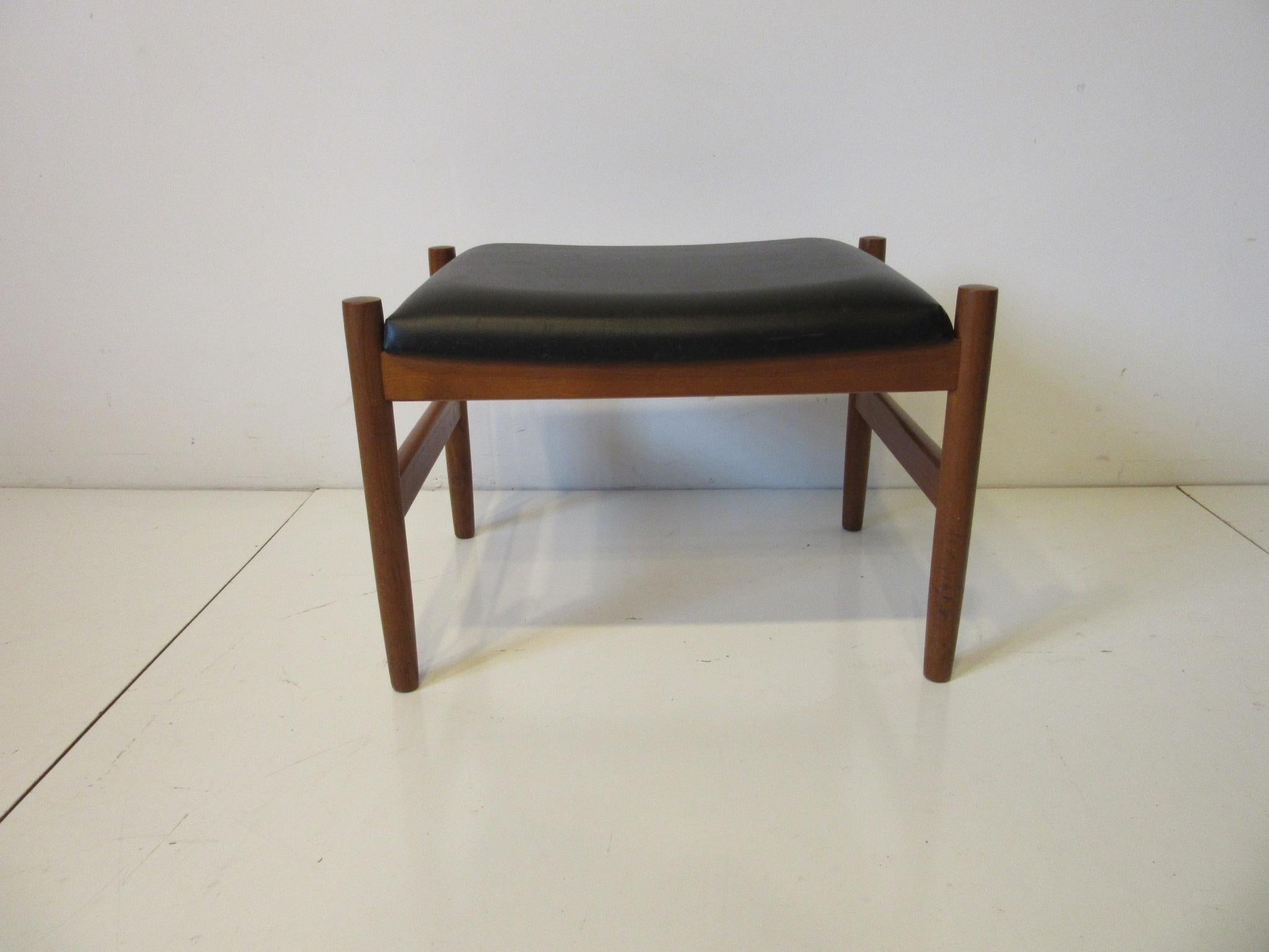 A nice simple well crafted teak framed foot stool with upholstered top in satin black leatherette retaining the original label HF Spottrup made in Denmark.