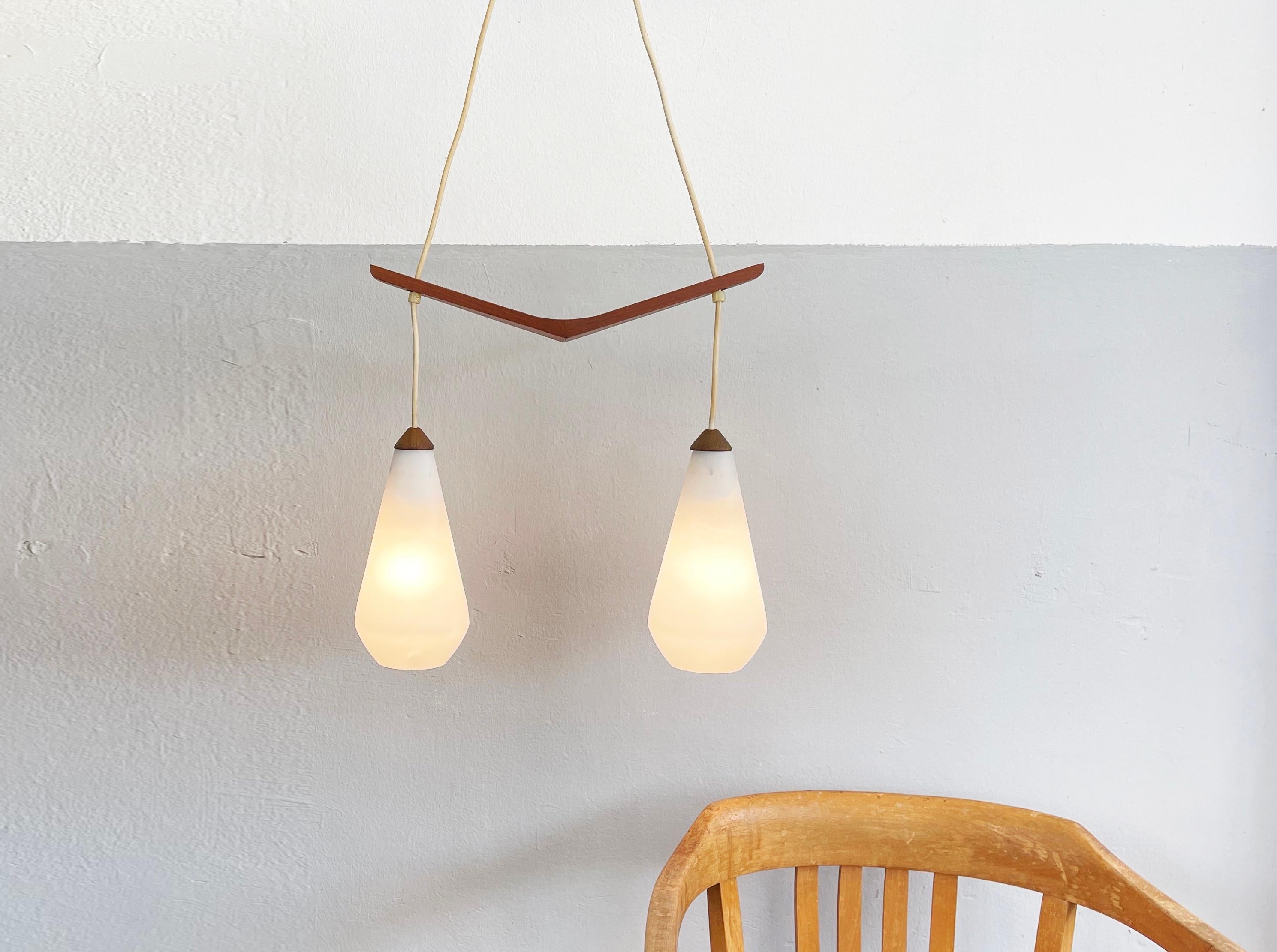 Lampe suspendue magnifiquement conçue par un artiste allemand du milieu du siècle, originaire du Danemark.
Verre opalin mat et soyeux (semi-brillant), les 2 abat-jour maintenus par du teck entièrement travaillé à la main.

Longueur du v-bar 15.74