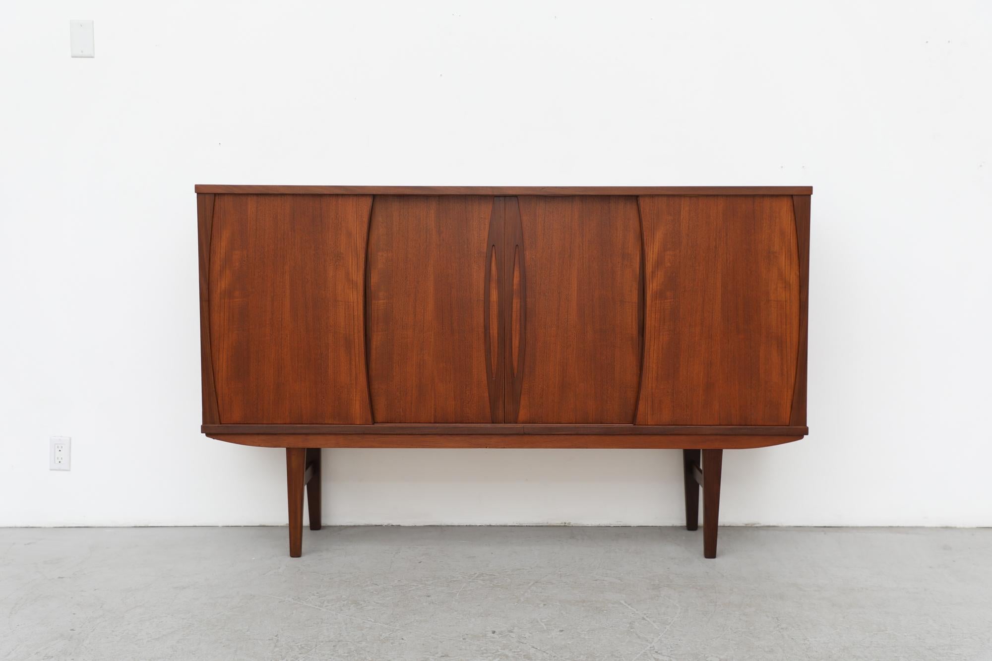 Danish Midcentury tall, teak sideboard with sliding doors and rosewood trim that reveal a Rat Pack style bar consisting of a mirror backed bar cubby with a pullout tray and 3 lower drawers. In original condition with a chip on the interior mirror.