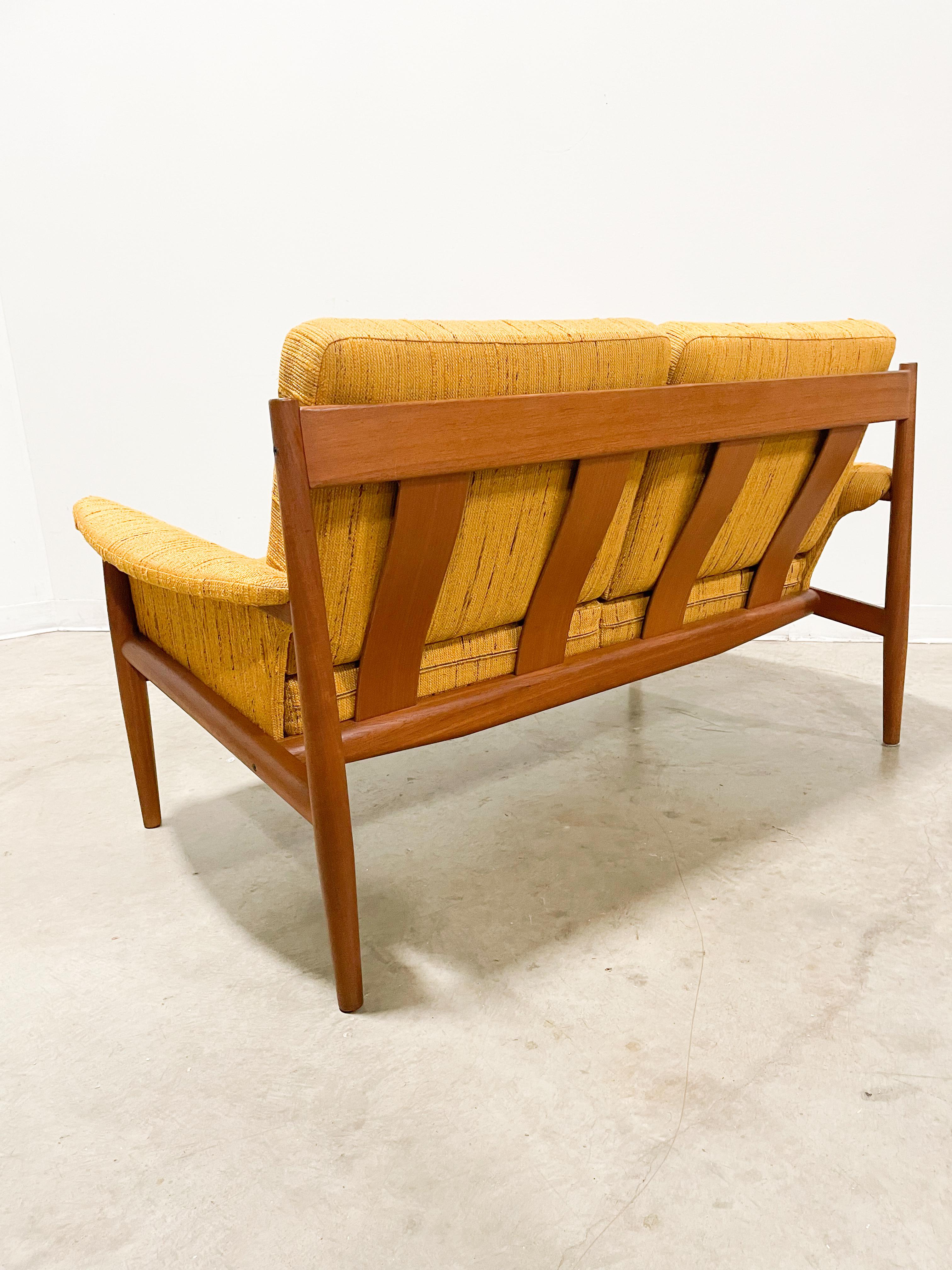 This beautiful love seat with original fabric and sprung cushions on a sculptural solid teak frame was designed by Grete Jalk and made in Denmark by France and Son. It is structurally solid, with minimal signs of wear, and remains very comfortable.