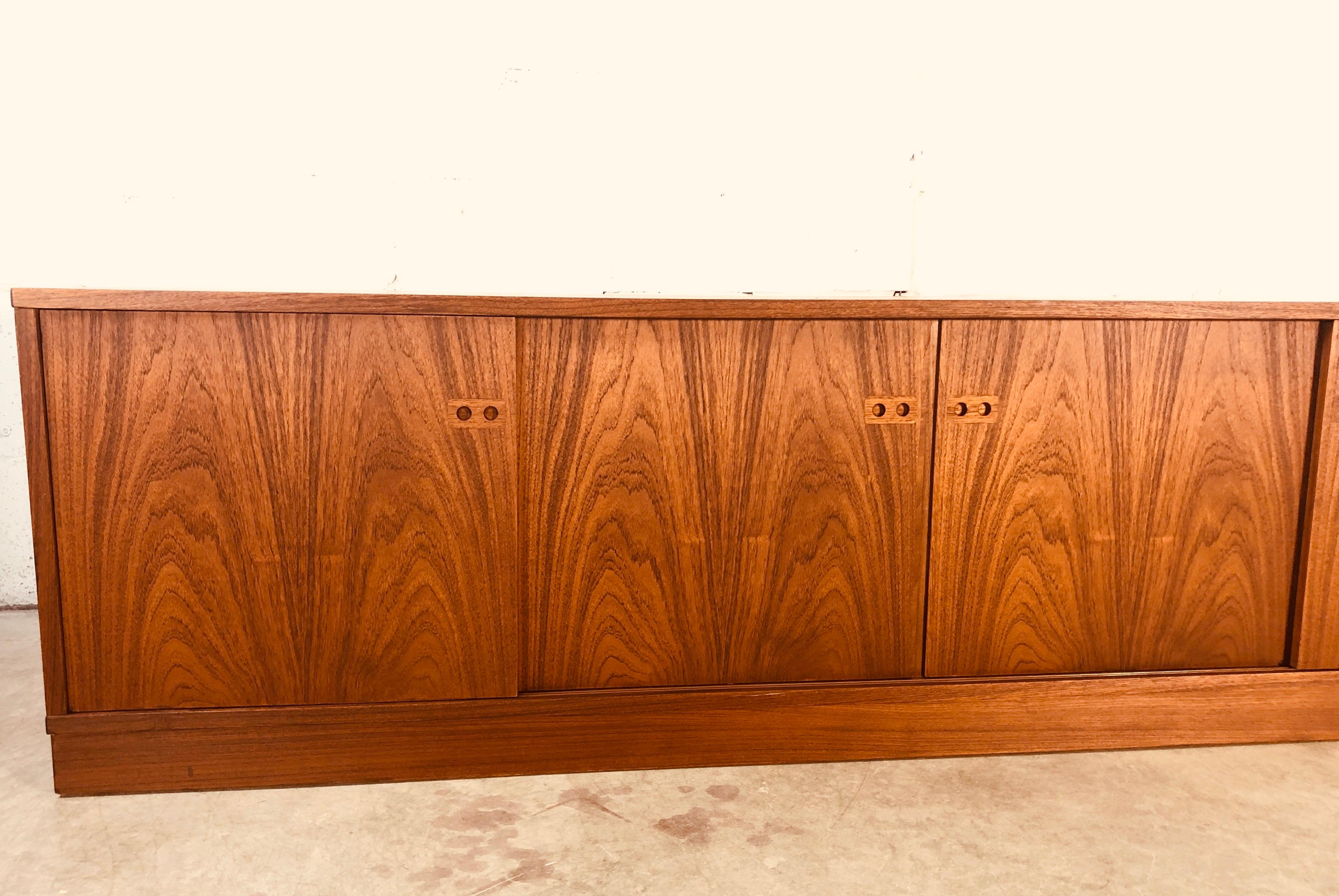 Mid-Century Modern 1970s Danish teak low slide front credenza. The credenza has drawer storage in the middle and additional storage on the sides. Newly refinished and in excellent condition. Back is finished and marked Made in Denmark.