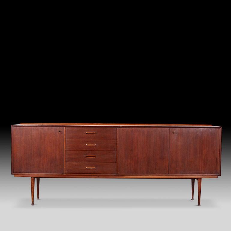 Elegant teak mid century sideboard, the slim case with three cabinets behind simple doors and with an offset bank of four drawers, the case raised on four turned tapering teak legs.
C. 1965.