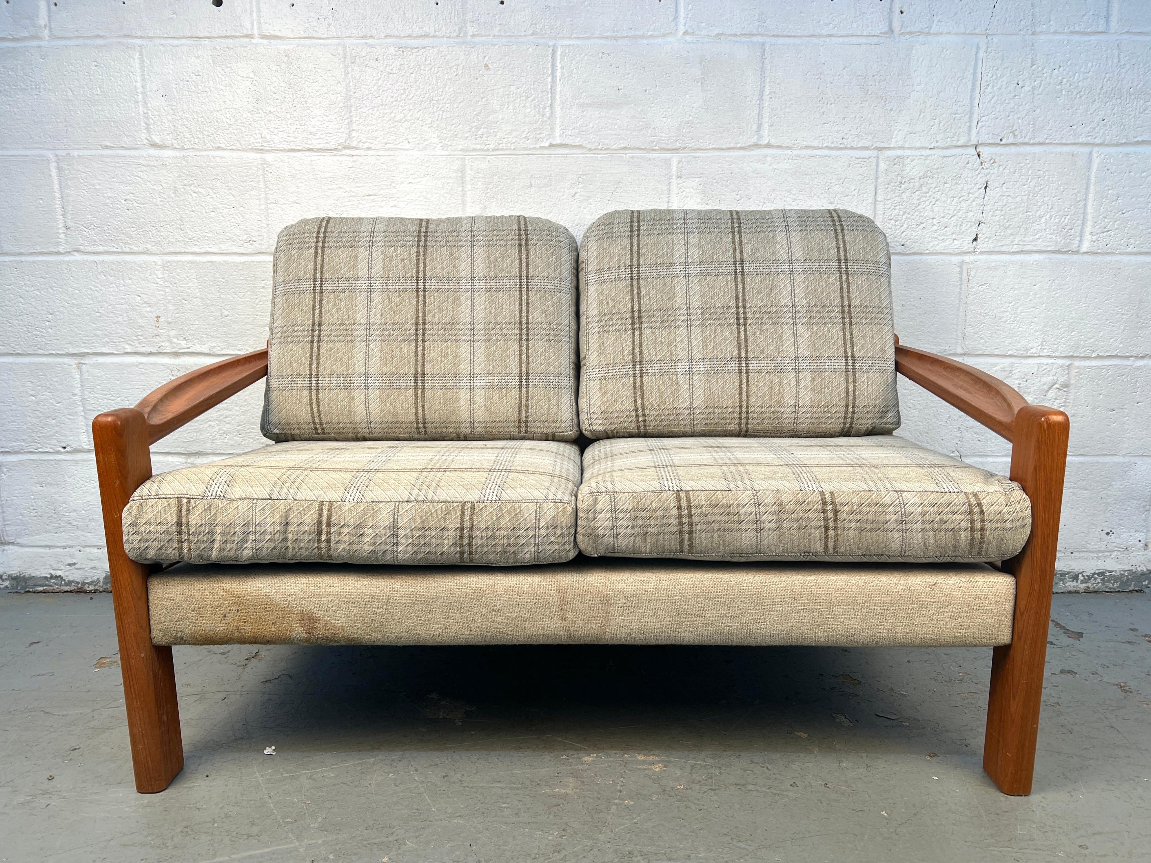 Un encantador sofá de dos plazas de teca danesa de mediados de siglo, con un armazón robusto y esculpido y líneas clásicas MCM. Los originales cojines de cuadros escoceses añaden un acogedor toque retro, manteniendo la comodidad y el carácter. Una