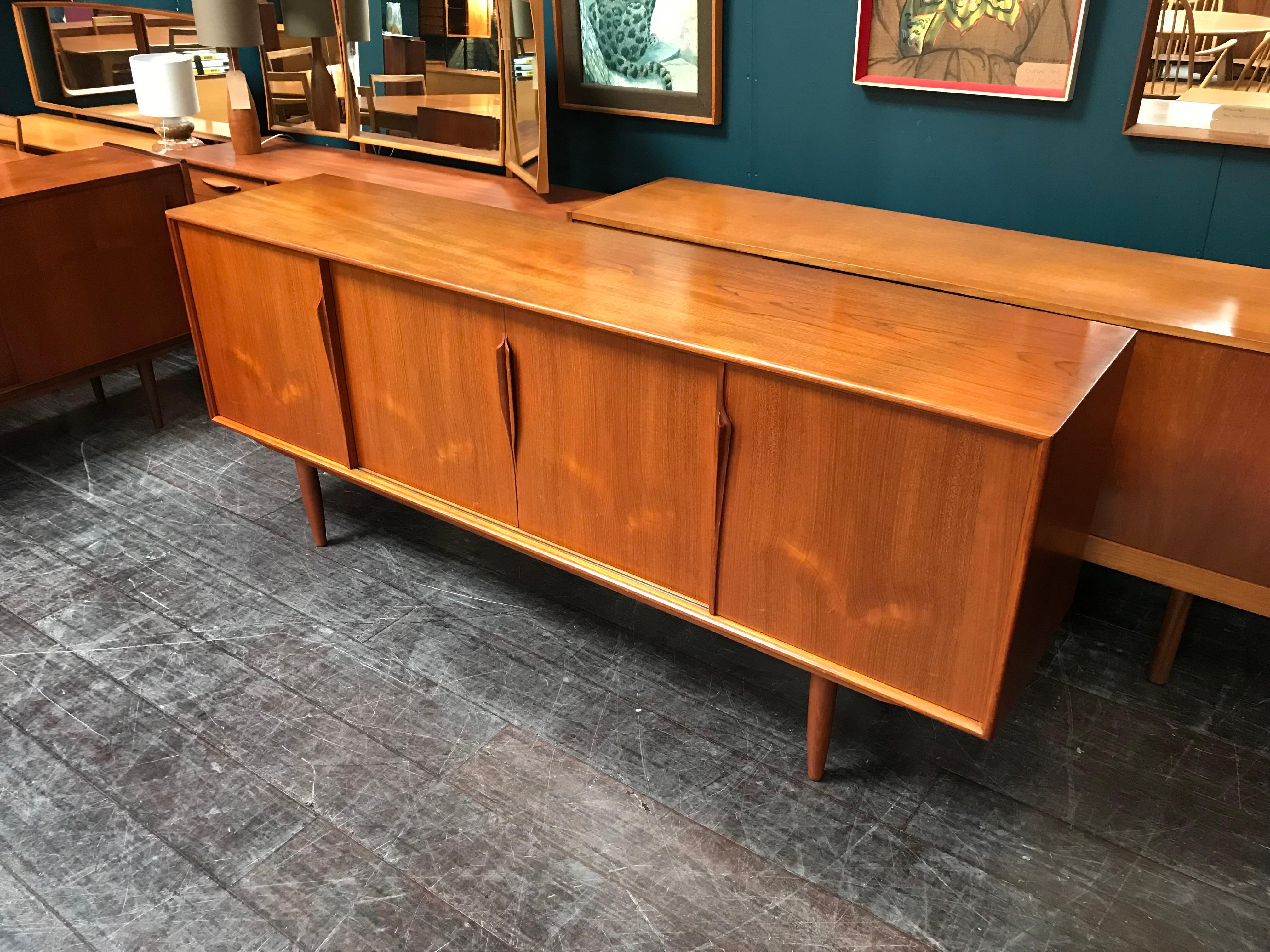 A fascinating teak sideboard produced in Denmark by the furniture maker Omann Jun and featuring sliding doors with three felt-lined drawers hidden behind its sleek exterior. This model by Gunni Omann has those beautiful long ‘organic’ handles
