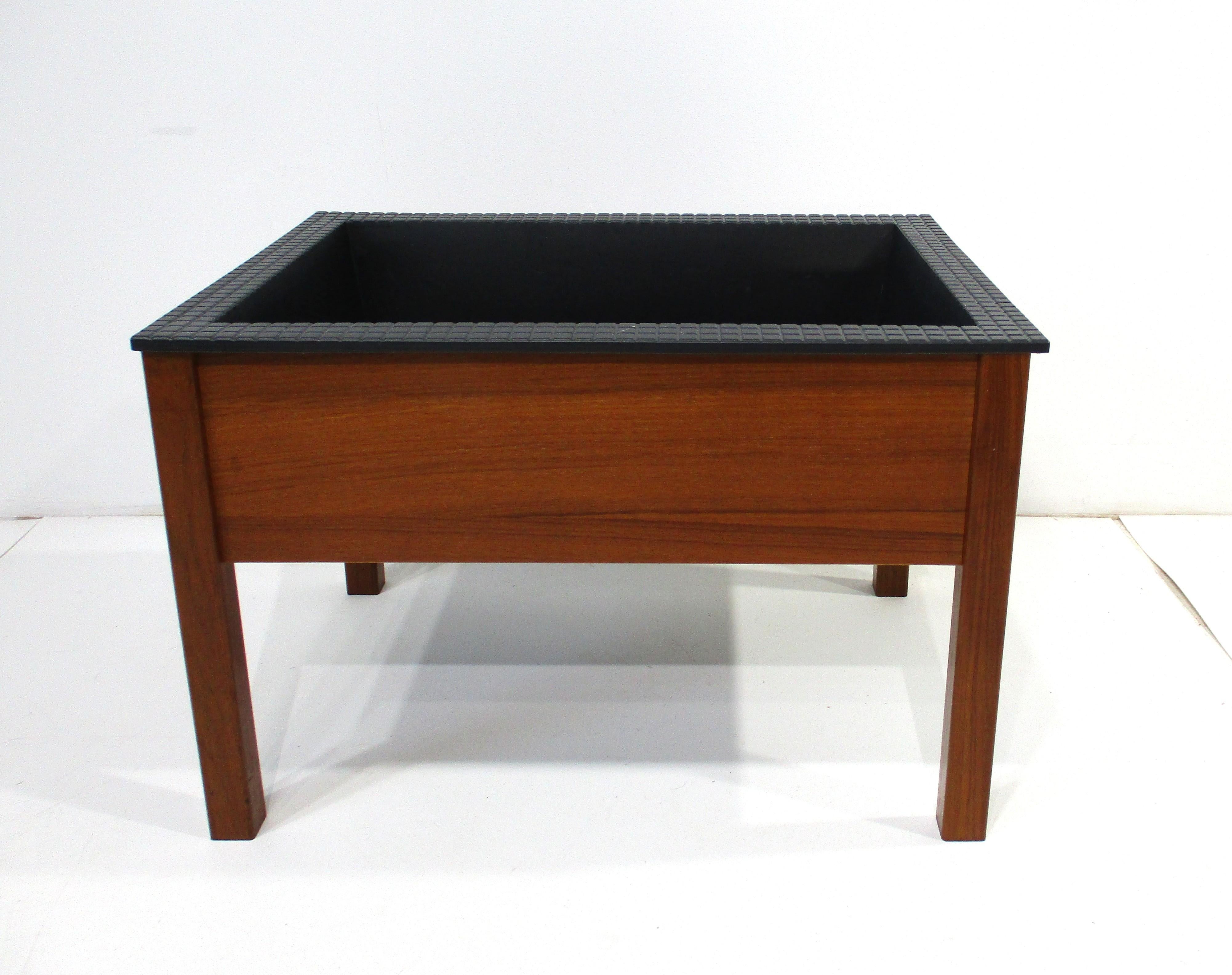Una maceta de madera de teca muy singular, con una pesada inserción de plástico negro satinado para las plantas, que se encaja en el marco cuadrado. Esta pieza bien hecha al estilo de Spottrup / Stolefabrik lleva un sello de tinta en el interior