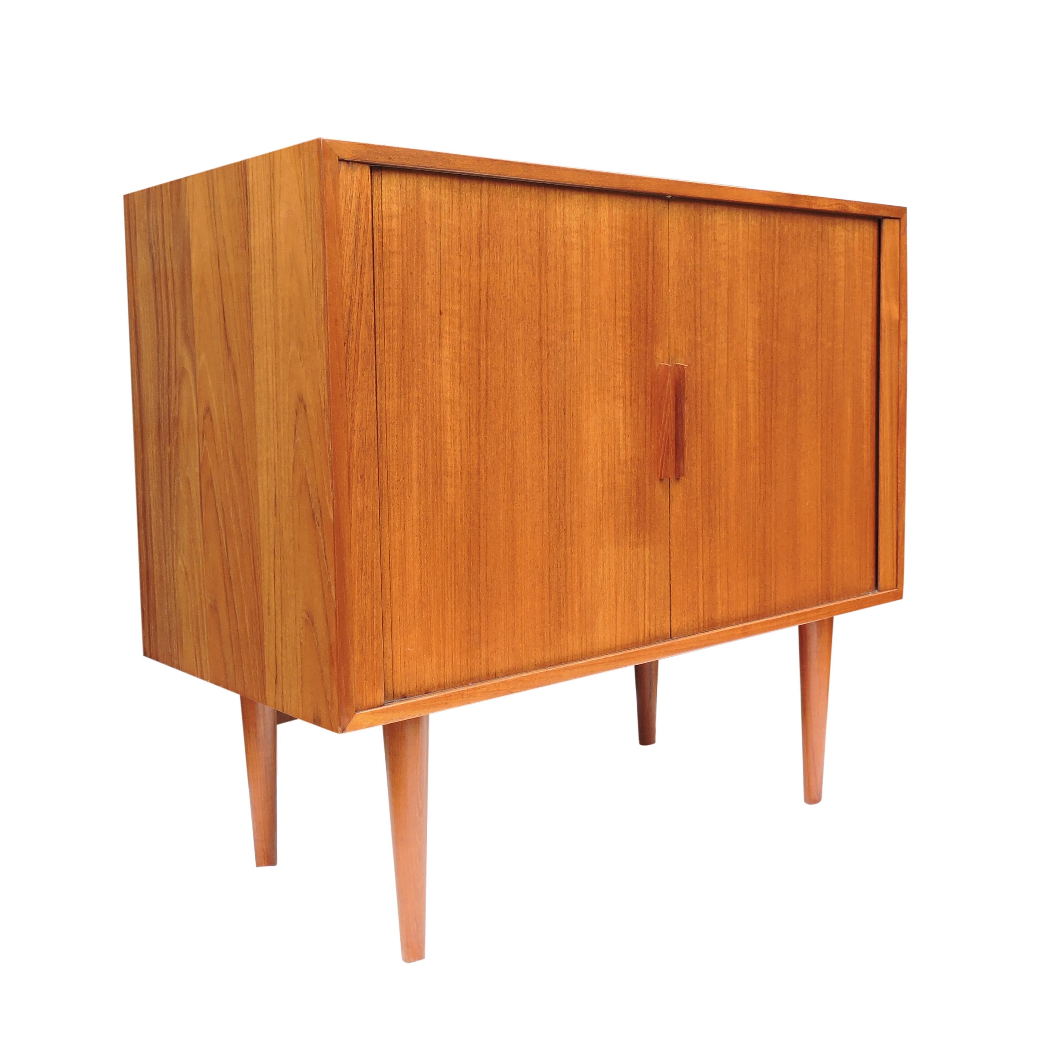 A teak tambour door record cabinet by Kai Kristiansen for Feldballes Mobelfabrik, Denmark, 1960s. There is divided space within, for records or books with two lower shelves.