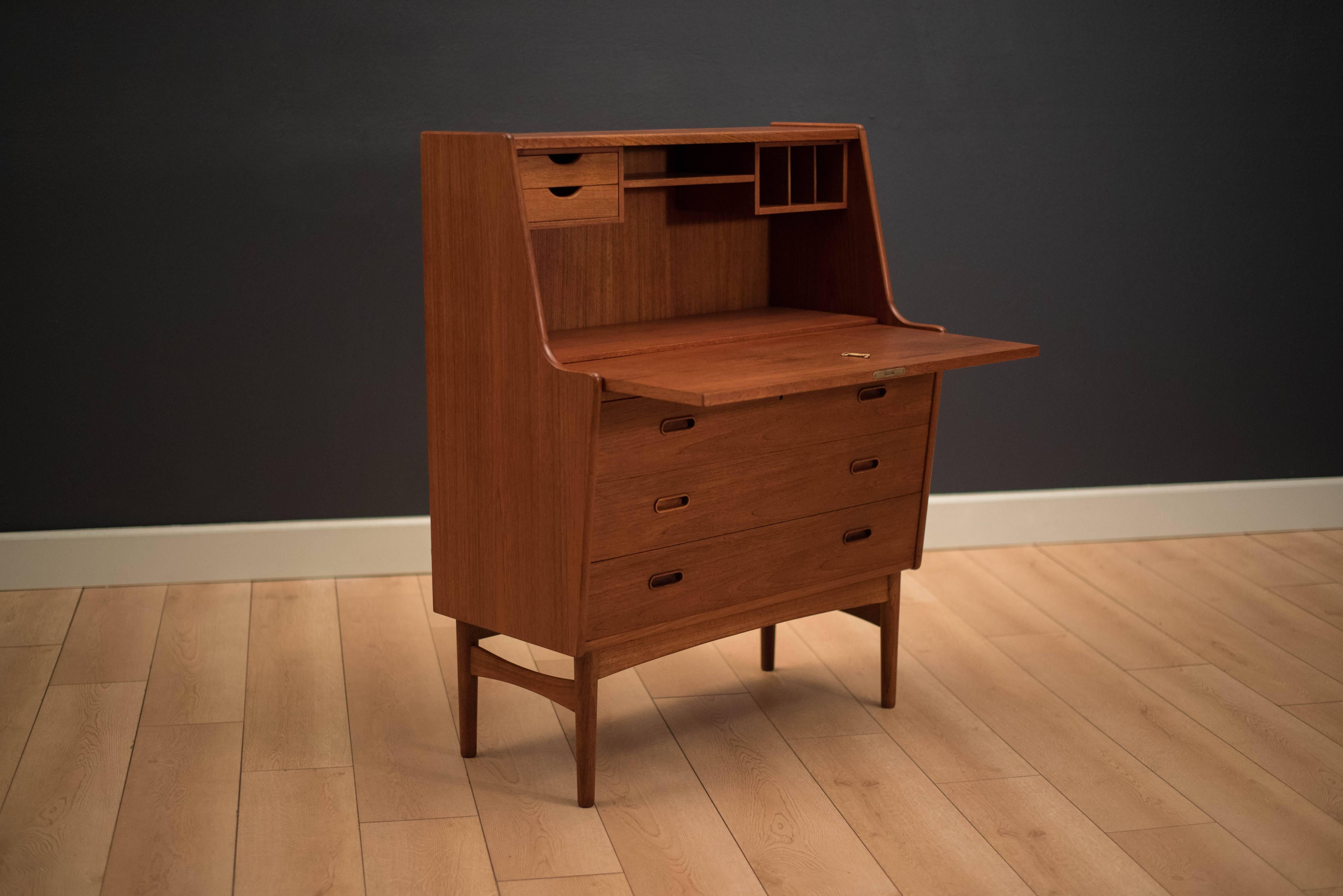 Danish Modern secretary desk designed by Arne Wahl Iversen in teak. This piece displays a beautiful teak grain facade and sculpted wood pulls. Equipped with three storage drawers and hidden compartments behind drop front door. Includes the original