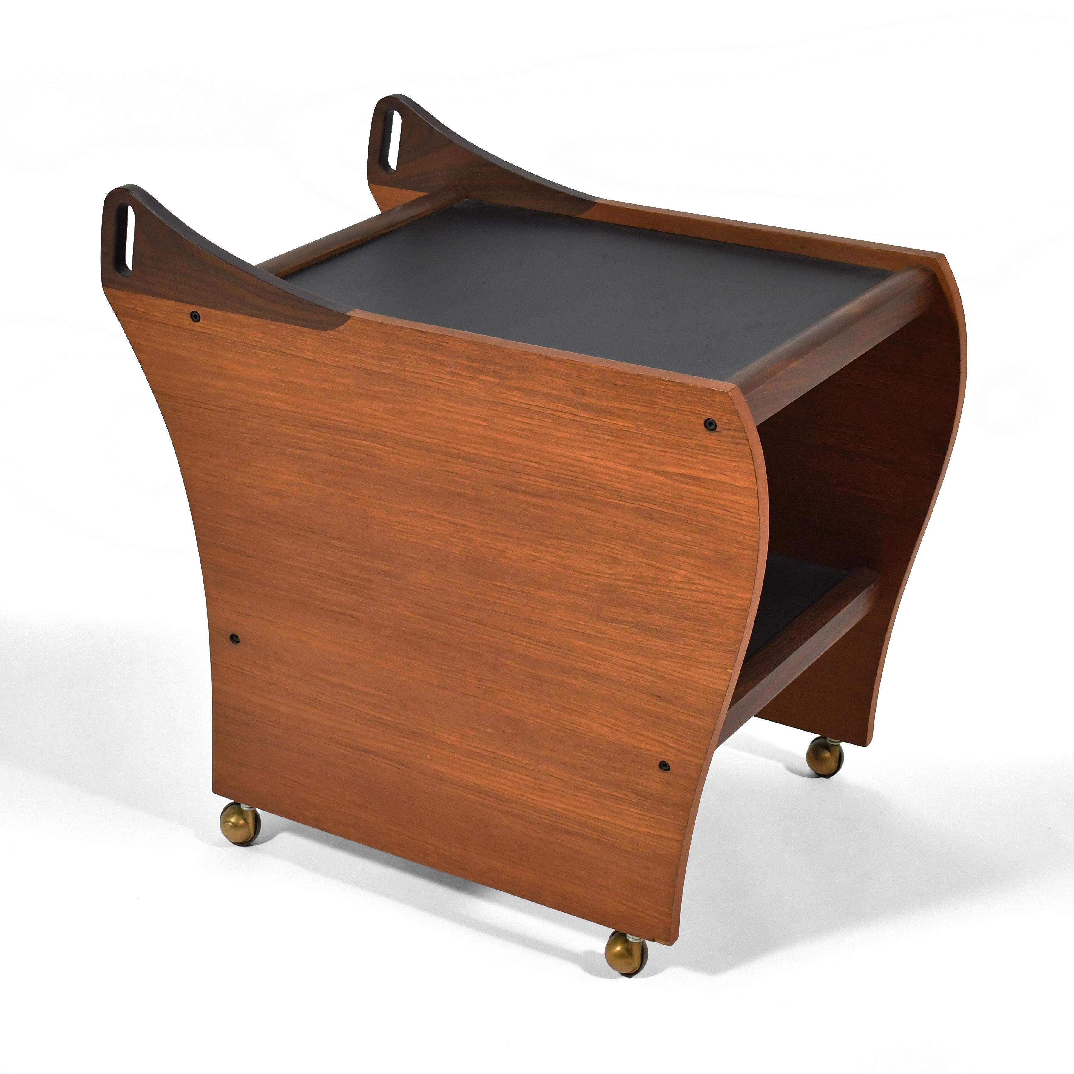 With two surfaces, casters, and handles to steer it, this beautiful teak cart is perfect as a serving or bar cart. The sculpted sides with flowing lines and integrated handles offer an opaque  contrast to the open, transparant front and