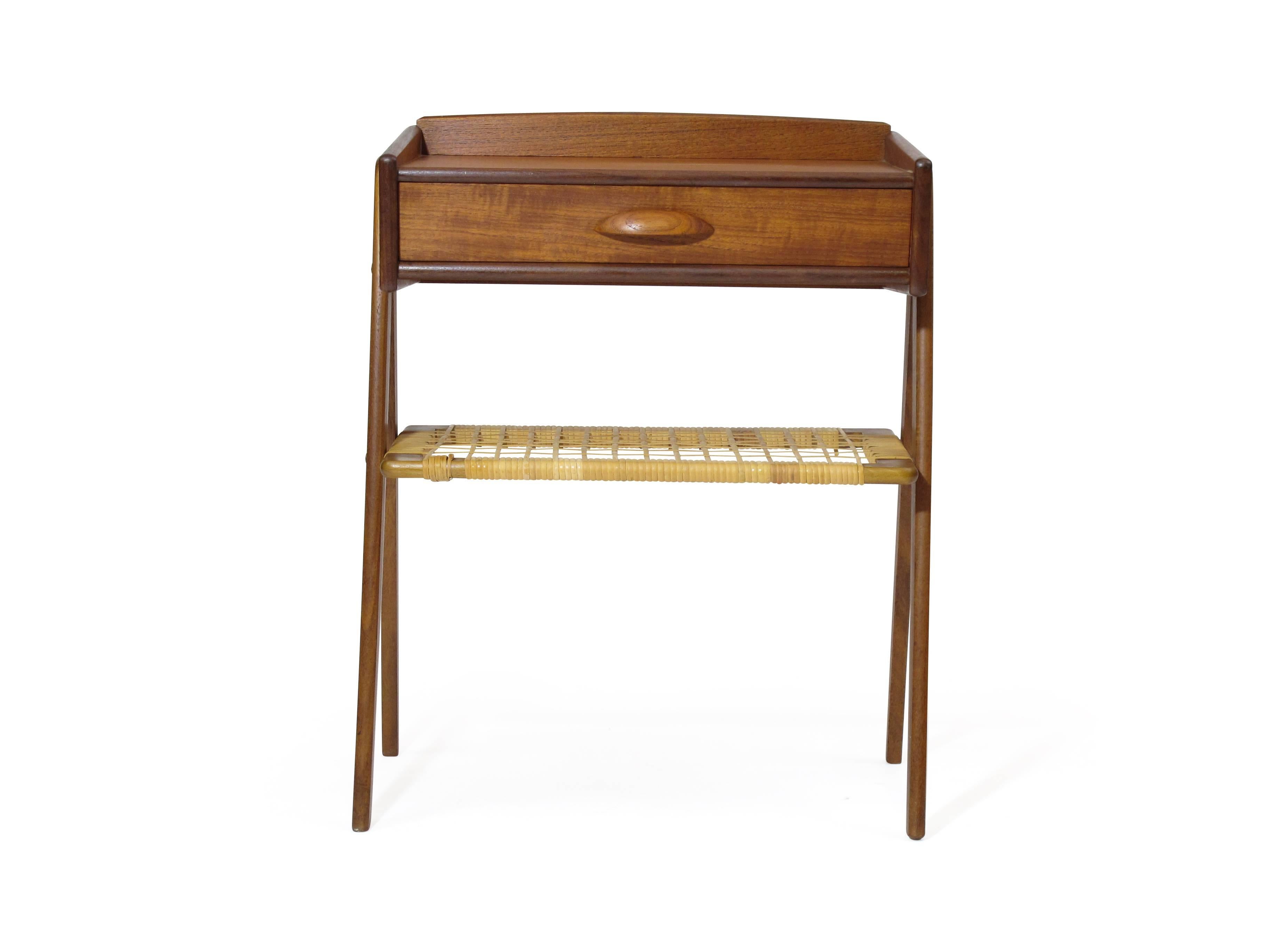 Midcentury Danish side table with one drawer and cane shelf under raised on angled solid teak legs.
