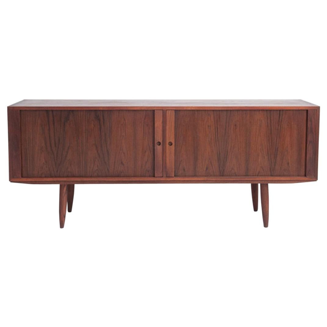 Astonishing sideboard made of veneered teak. Front with two tambour doors enclosing eight varnished pullout trays. Round tapered legs. Produced by Bruno Hansen Snedkerier, Slagelse Denmark.