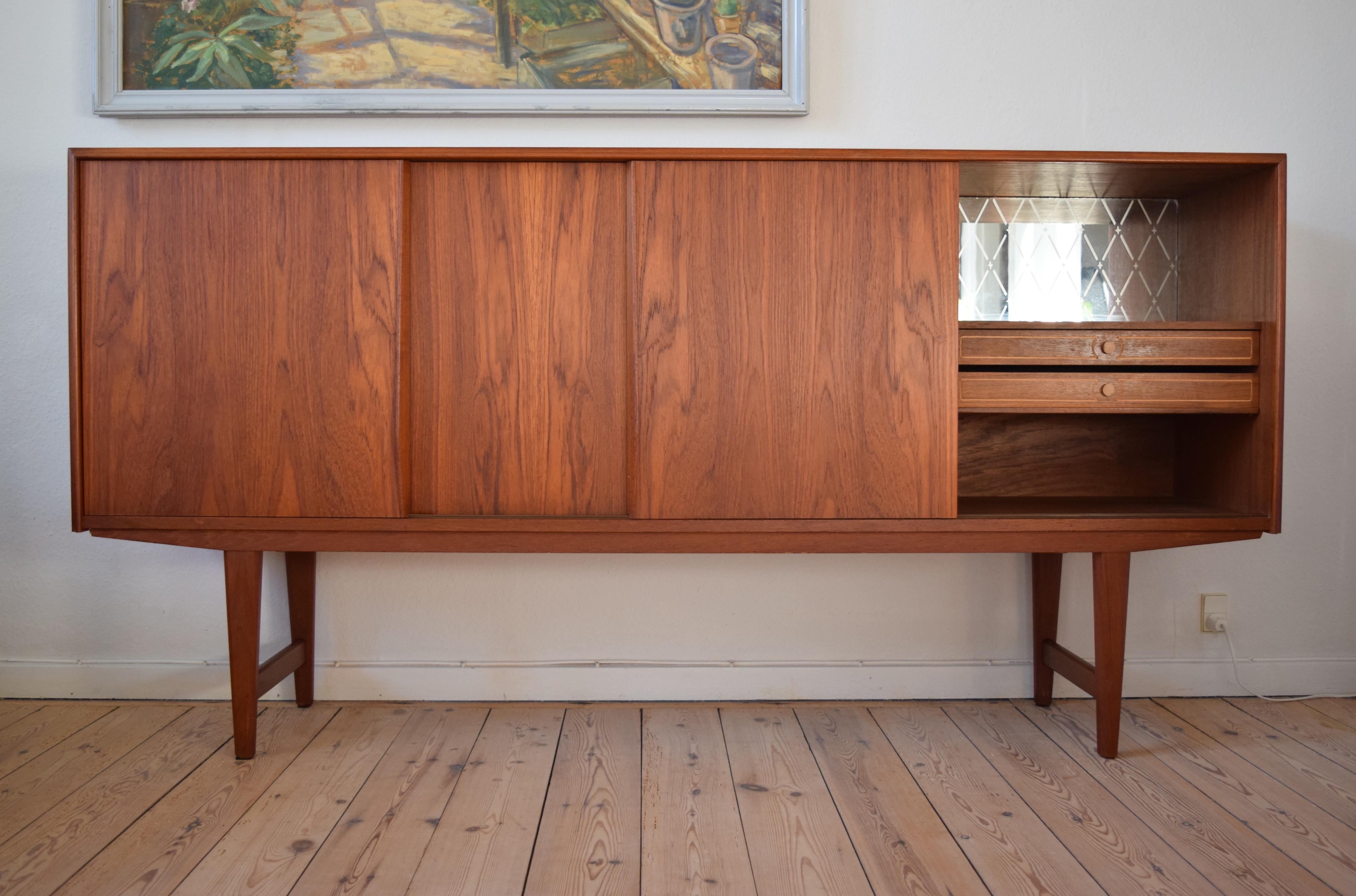 Low teak sideboard deigned by E.W. Bach manufactured in Denmark in the 1960s. Four smooth sliding doors on the front with three internal compartments with shelves. A small ducting channel has been covered over in the centre compartment, though this