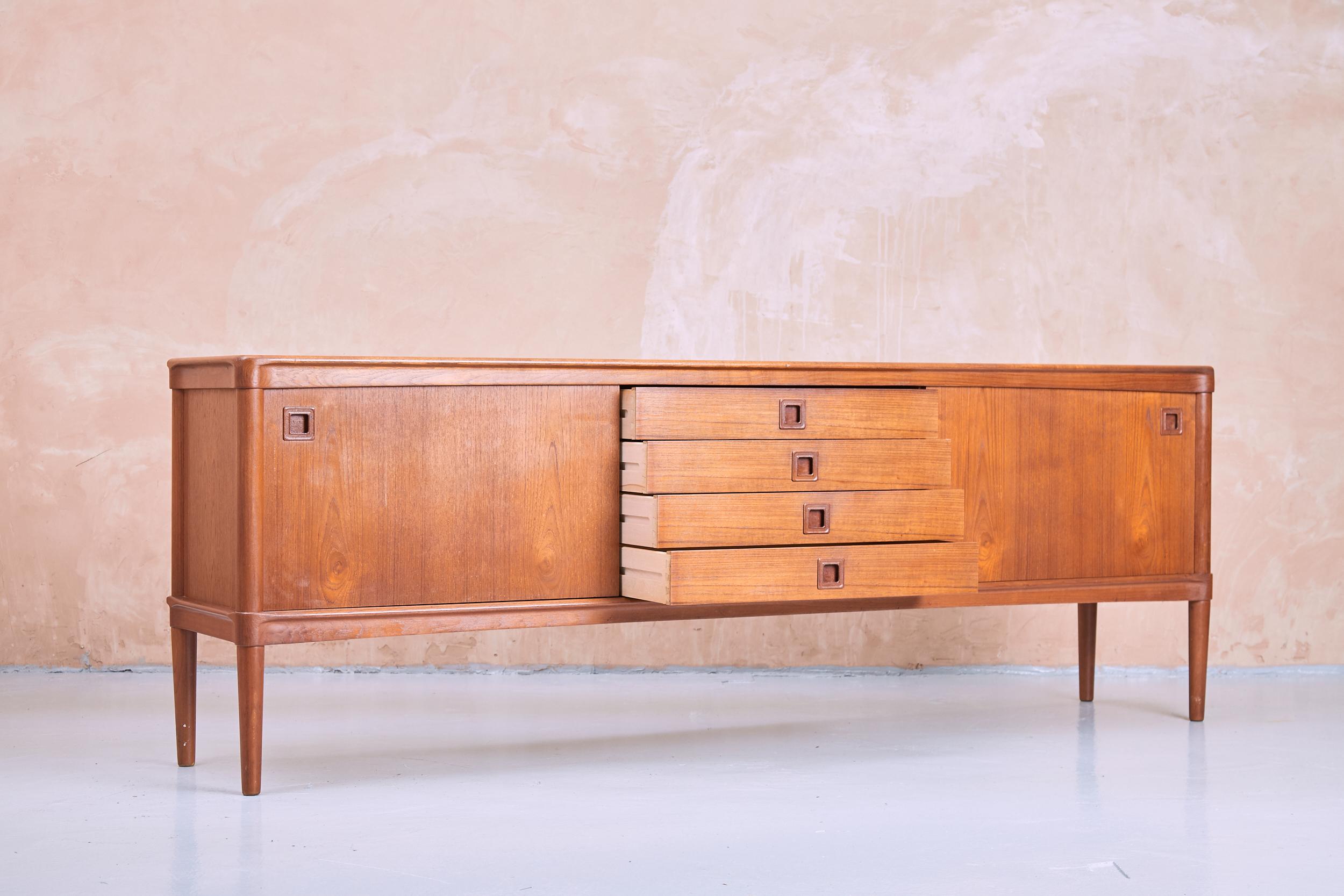 A Danish sideboard designed by Henry W.Klein and produced by Bramin in the 1960s. Crafted in teak, this statement piece features four centre drawers and two large sliding cupboard doors. All doors and drawers feature the designer’s signature carved