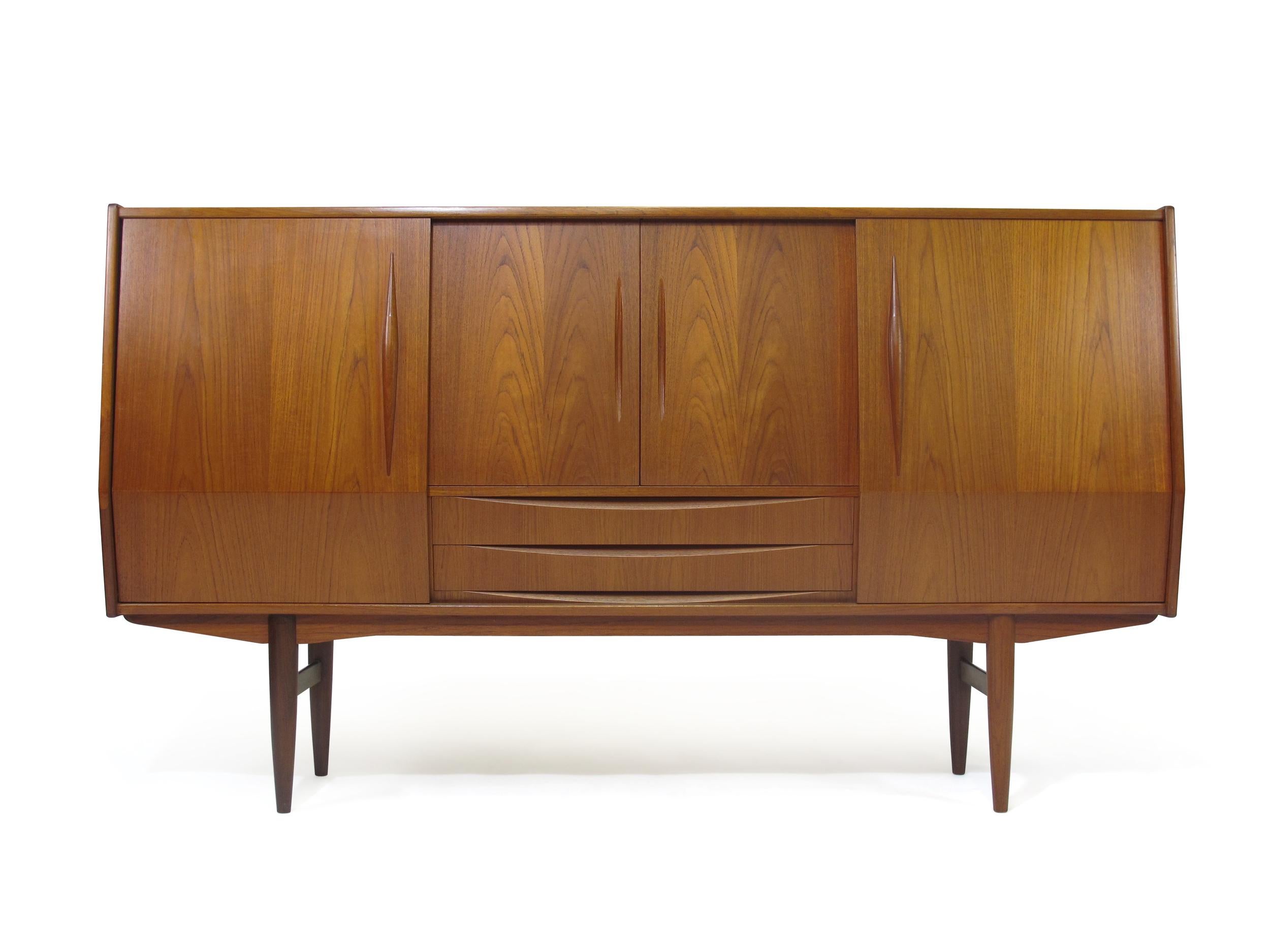 Scandinavian teak high sideboard cabinet with dramatic angled sliding doors. Interior consists of adjustable shelves and a mirrored back bar in rosewood with felt lined silverware drawers. Cabinet has been lightly cleaned and oiled and in very good,