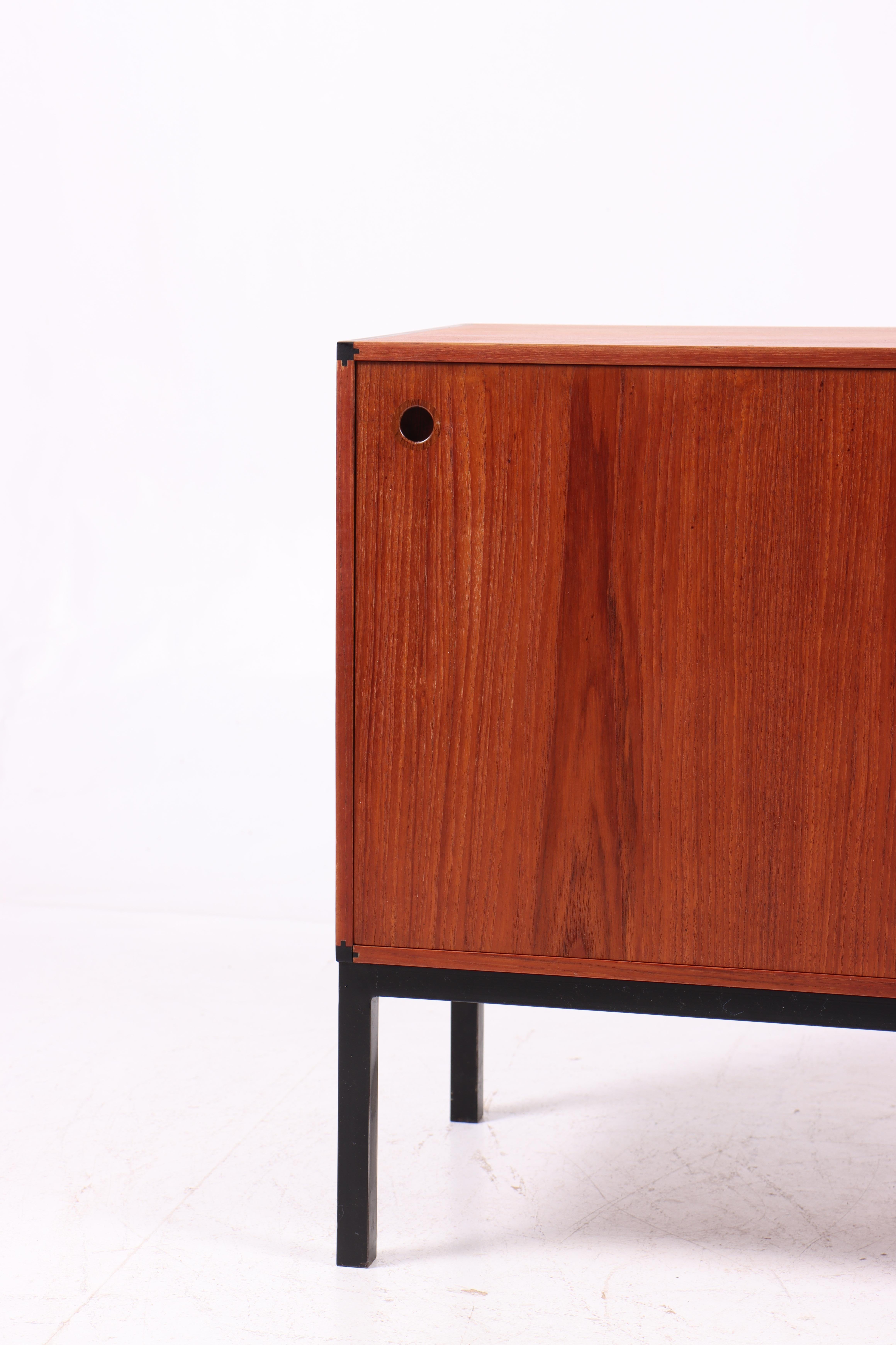 Elegante credenza danese moderna in teak, progettata e prodotta in Danimarca negli anni '60. Il mobile è dotato di due ante scorrevoli con maniglie circolari incassate e poggia su una base minimalista in metallo laccato nero - un contrasto