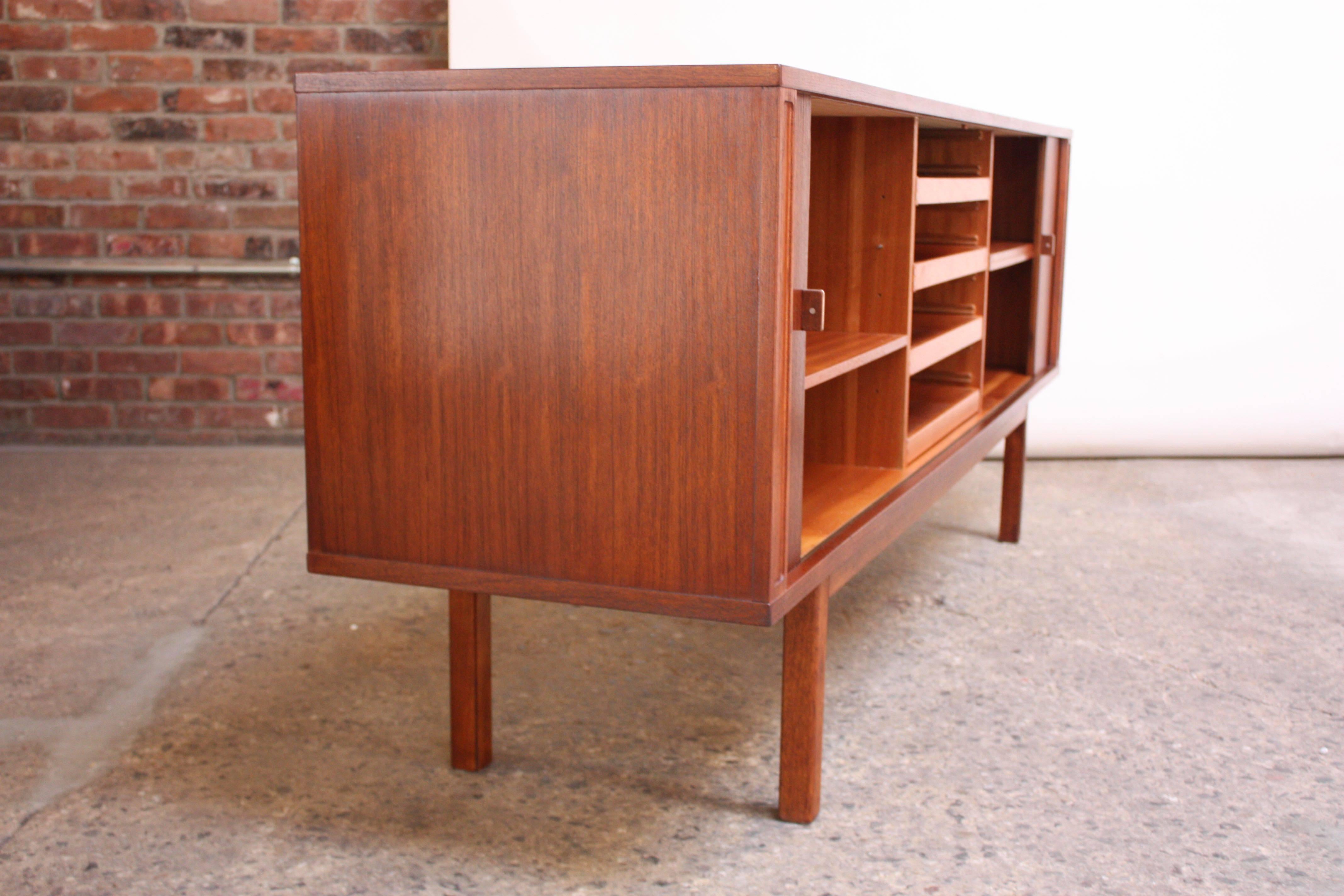 This teak sideboard was designed and manufactured by Peter Løvig Nielsen in 1976. The tambour doors slide open to reveal three sections: Open storage to the left and right divided by a total of three adjustable shelves and four centre drawers (one