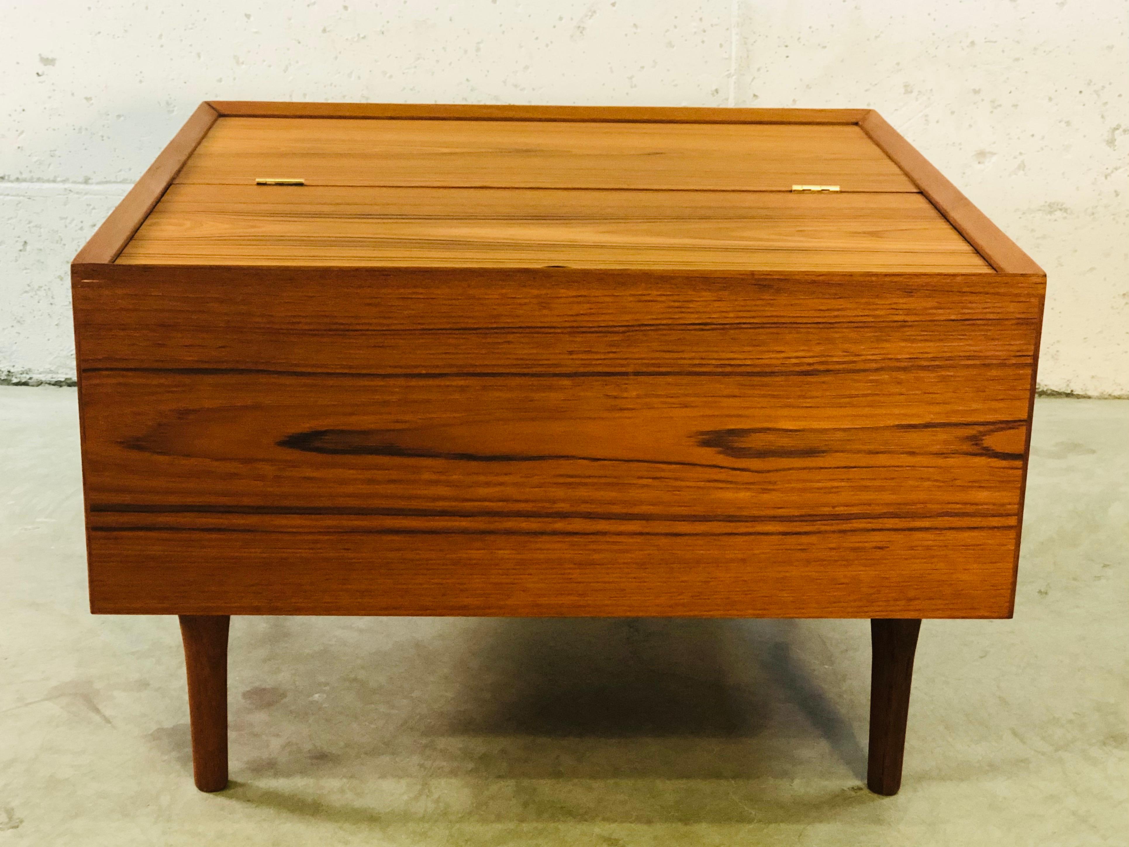 Vintage 1960s Danish teak square storage coffee table with flip top door. The table has a birch wood interior and round teak legs. Lots of interior storage room and one side flips up to reveal the opening. No marks. Refinished condition.