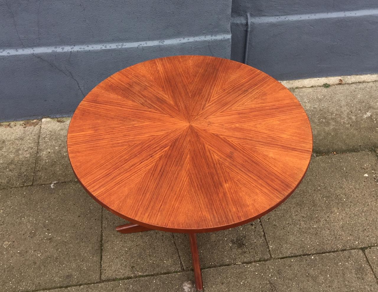 This midcentury Danish teak coffee table comes with sculptural solid teak legs and intricate veneer work in the shape of a bursting star on the tabletop. It is commonly referred to as the Starburst coffee table. It was designed by Holger Georg