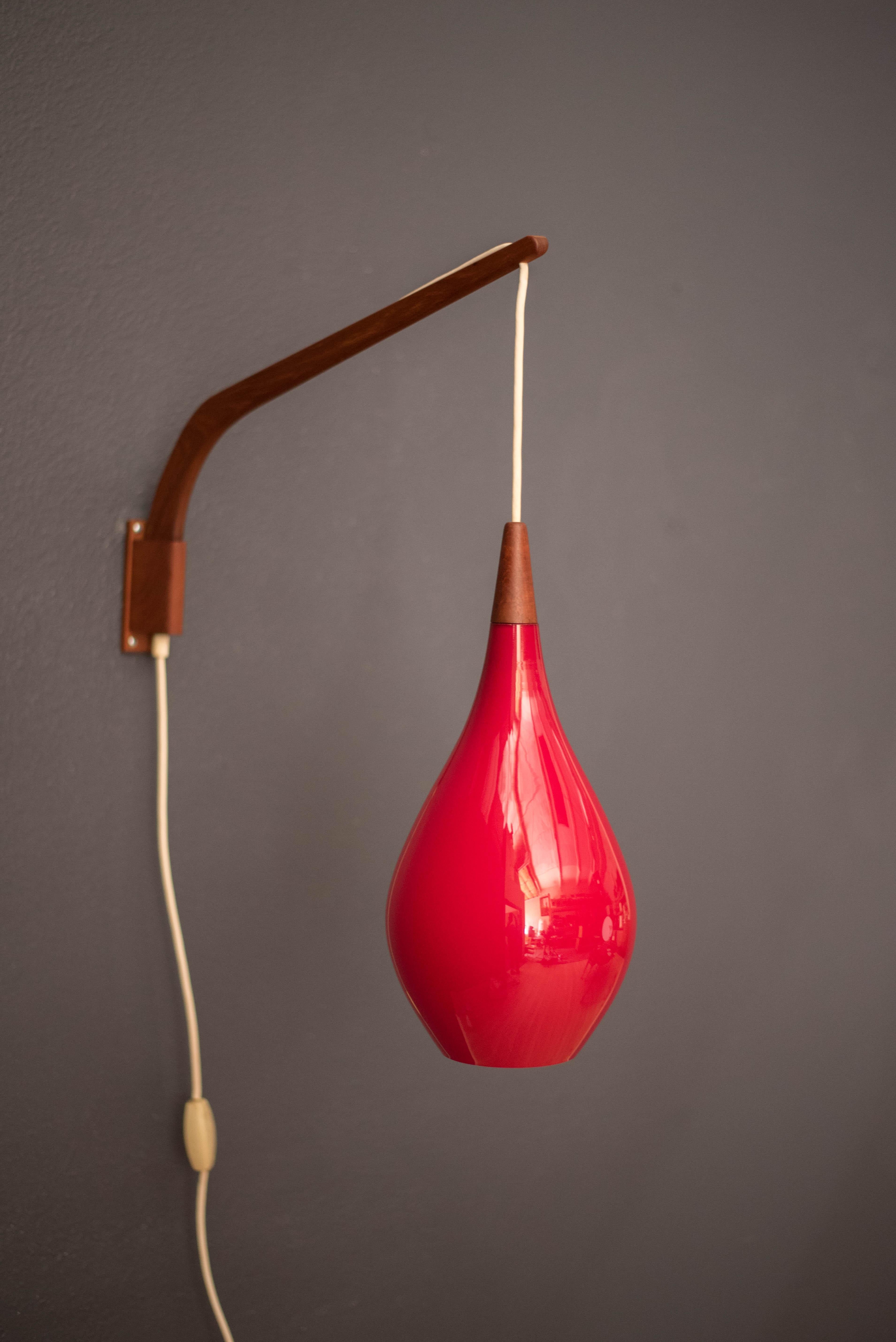 Mid-Century Modern hanging wall light by Holmegaard circa 1960's, Denmark. This piece displays a candy red teardrop glass shade with a frosted white interior. Includes a teak swivel arm with an adjustable cord. 

Swing arm 24