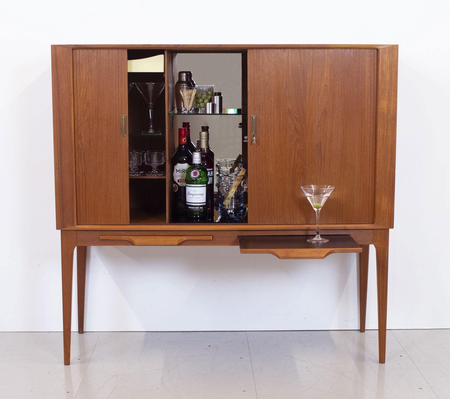Fabulous and elegant 1960s Danish teak drinks cabinet designed by Illum Wikkelsø for C.F. Christensen Silkeborg.  Beautifully made and with lots of interesting details, it features tambour doors with brass handles and key, two pull out Formica