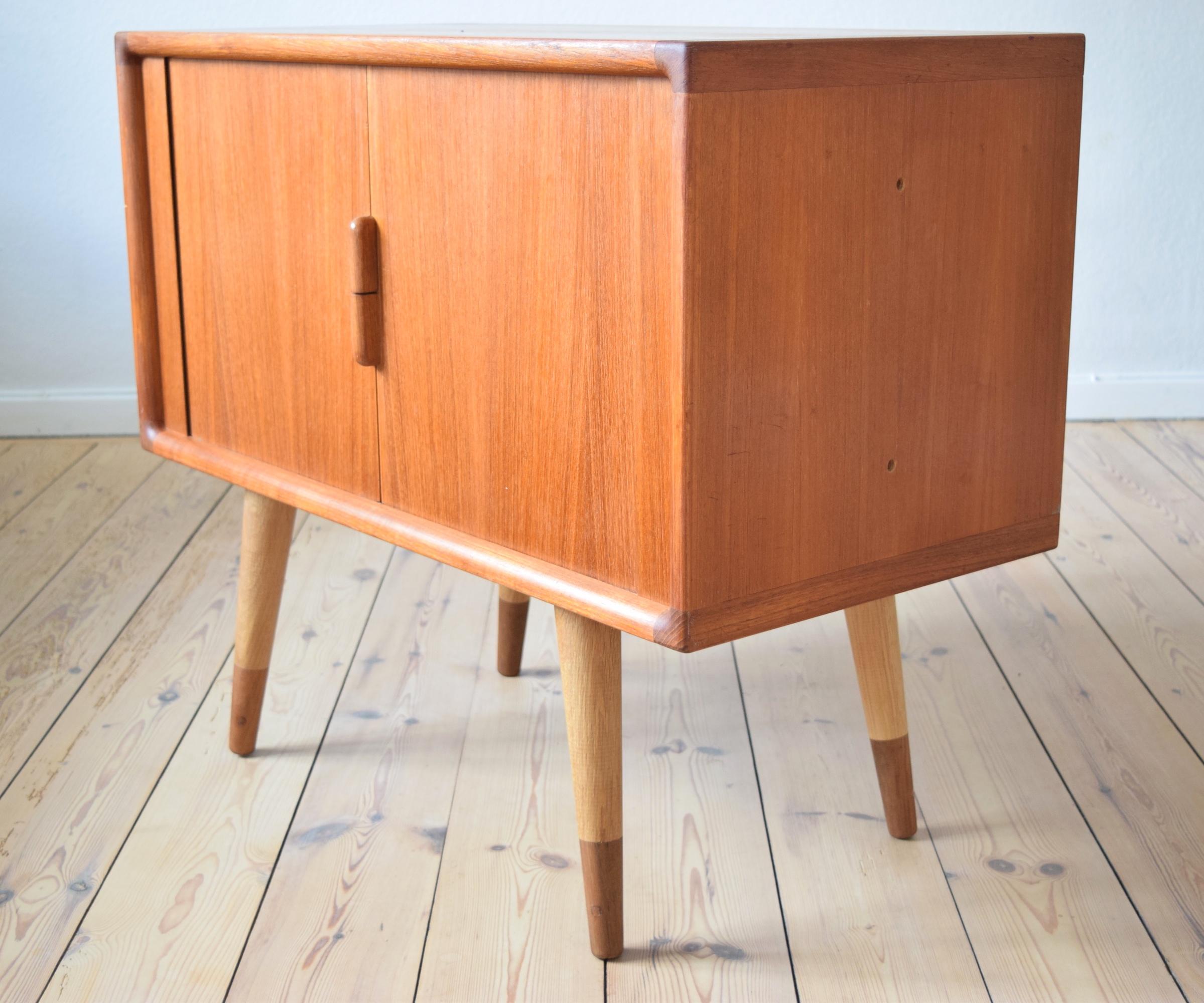 Teak cabinet with tambour doors manufactured in Denmark in the 1960s. This piece features internal shelf and teak sliding drawer. Bevelled edge all round. Originally sat on a plinth. Legs added at a later date using a combination of teak and oak.