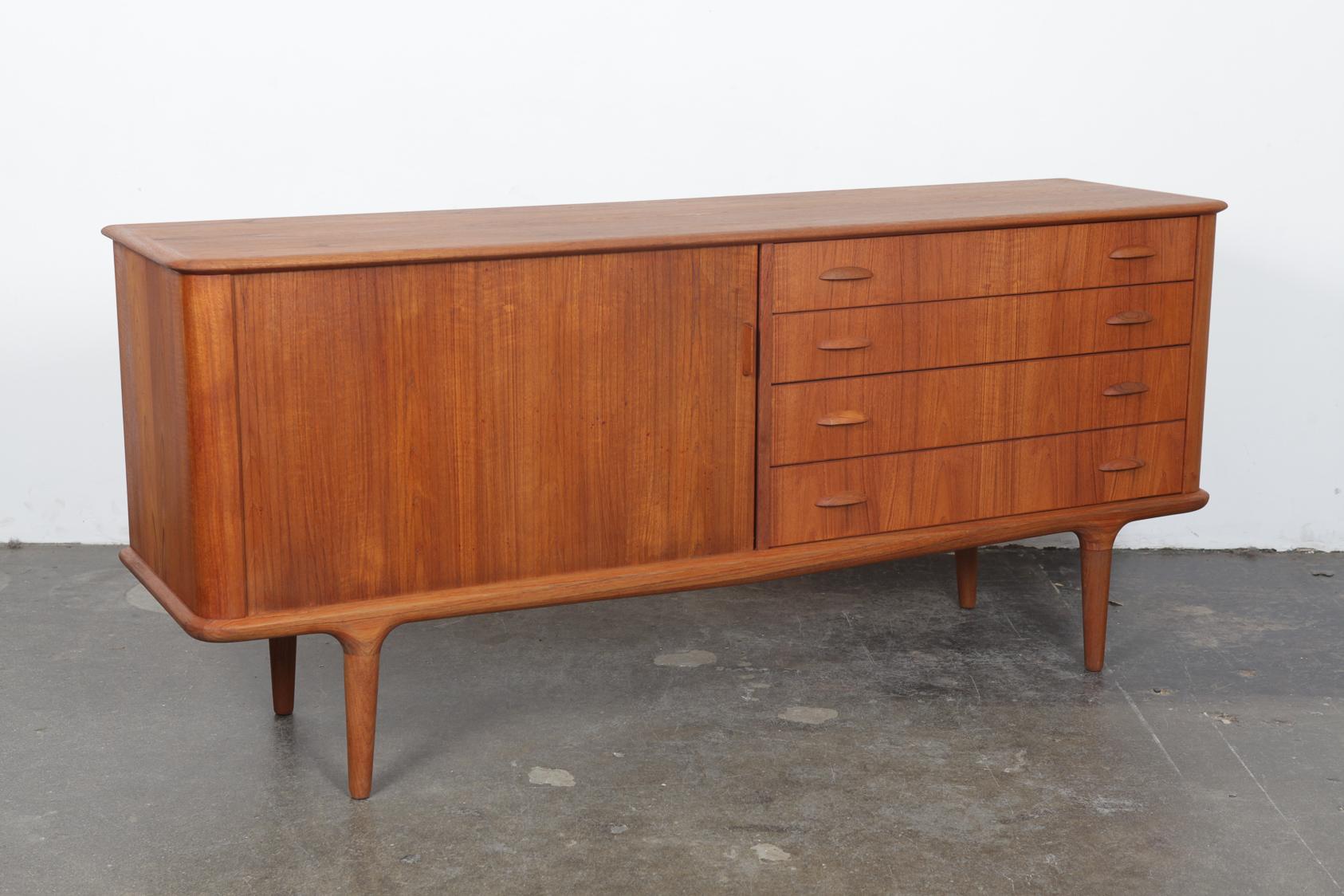 Newly refinished Danish Mid-Century Modern beautiful teak tambour door sideboard with four drawers and a rounded front and side edge on solid teak tapering legs. Drawers have half shell-style pulls. Designer made I'm not just sure of who the