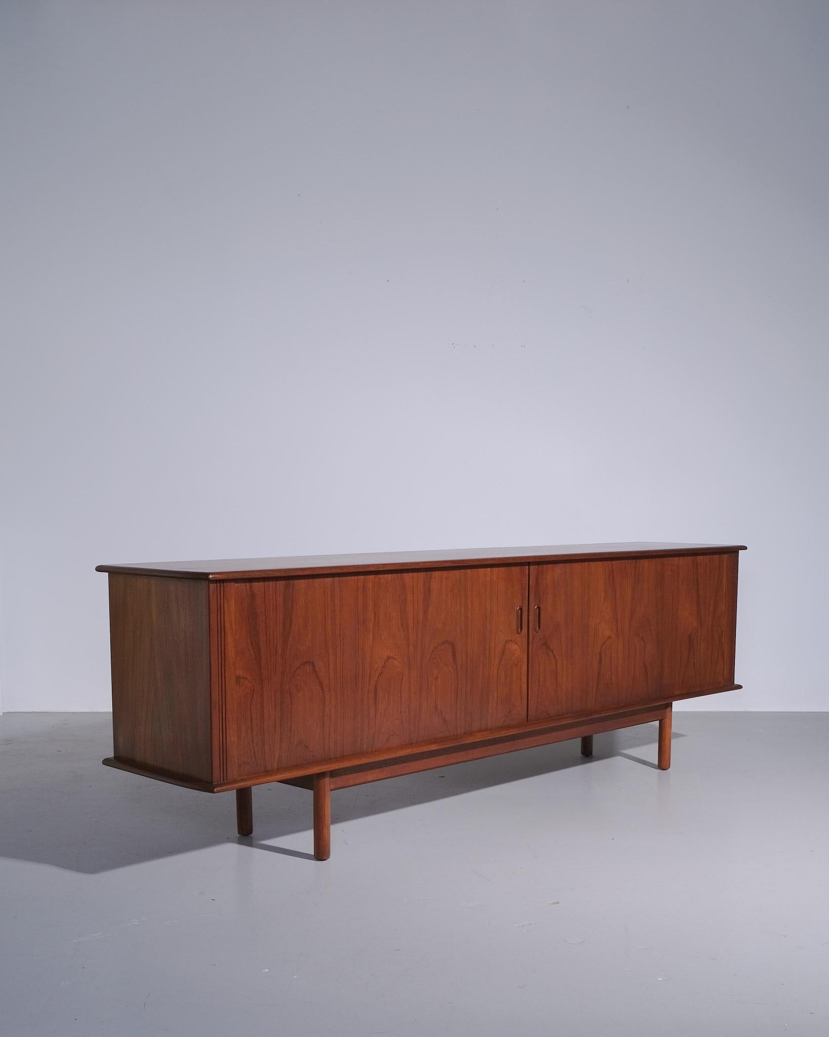 Classico esempio di artigianato danese di metà secolo, questa credenza tamburata in teak risale agli anni '50 e mette in mostra l'estetica raffinata e funzionale che definiva il design scandinavo dell'epoca. La silhouette lunga e bassa è bilanciata