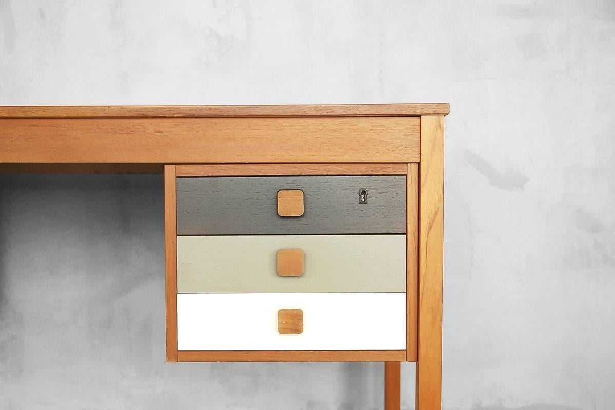 This vintage desk was manufactured in Denmark by Domino Møbler during the 1960s. It is veneered in teak and has legs made of solid wood. This desk is fitted with six drawers with solid wood handles and fronts in pastel colors. The top drawers are