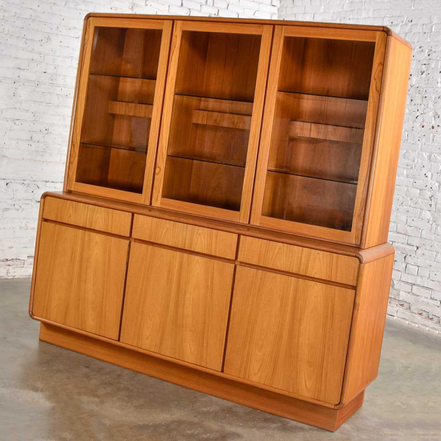 Magnificent Danish teak midcentury Scandinavian Modern two-piece lighted china hutch, and buffet. Comprised of three teak veneer bottom doors with inside teak shelves and the top hutch with three glass doors and two glass shelves per door (a total