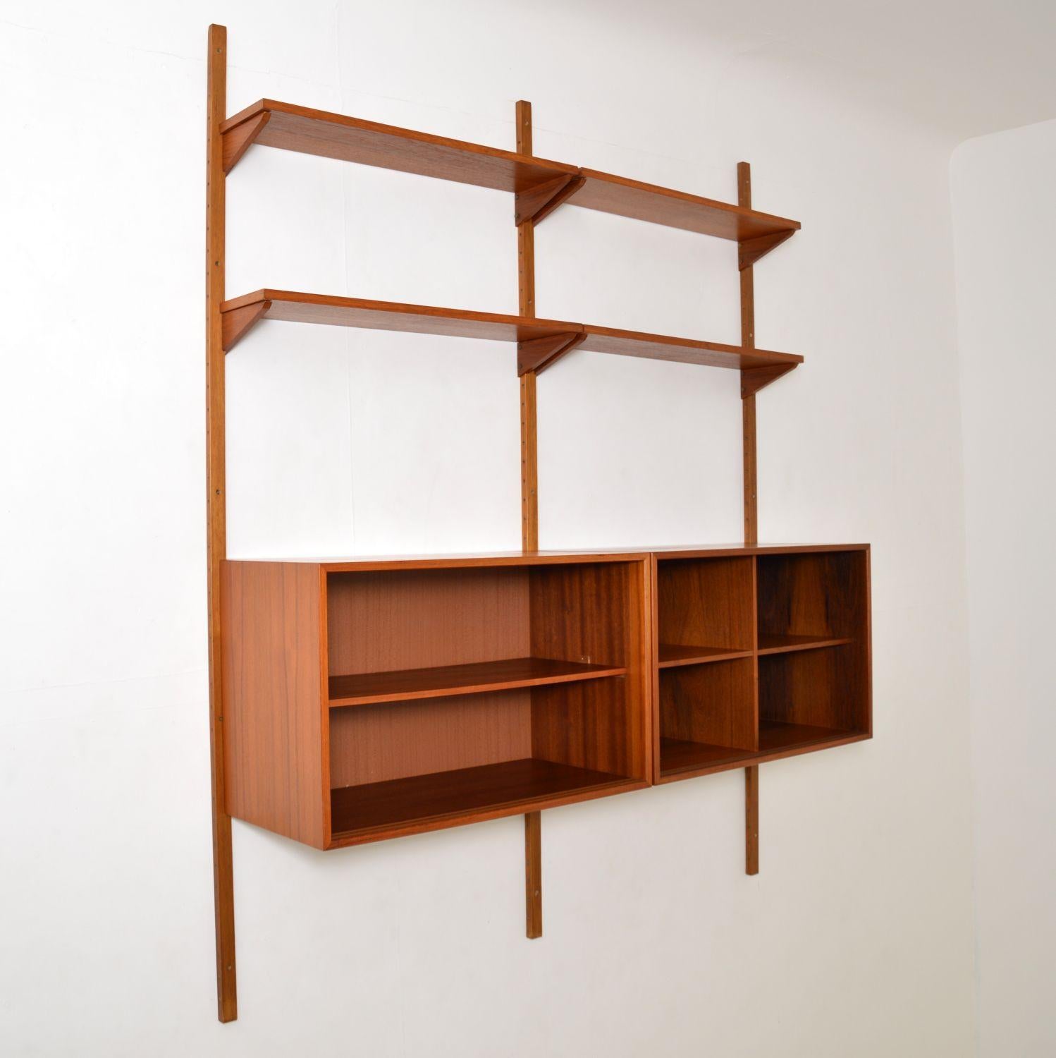 A stylish and versatile wall mounting cabinet in teak, this is the PS system, made in Denmark in the 1960s.

This double bay consists of two sliding door cabinets, four chevron supported shelves, and three long wall mounting rails. The cabinets