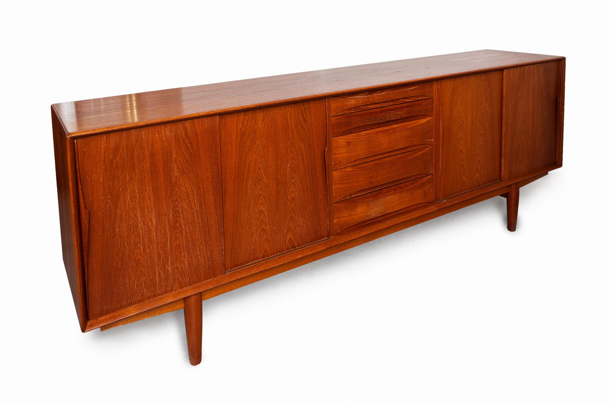 Vintage midcentury credenza by Skovby Mobelfabrik, Denmark. The front features two cabinets with four sliding door panels, each with carved vertical pulls and five dovetail drawers, two of which are lined with felt.
The subtle minimalistic details