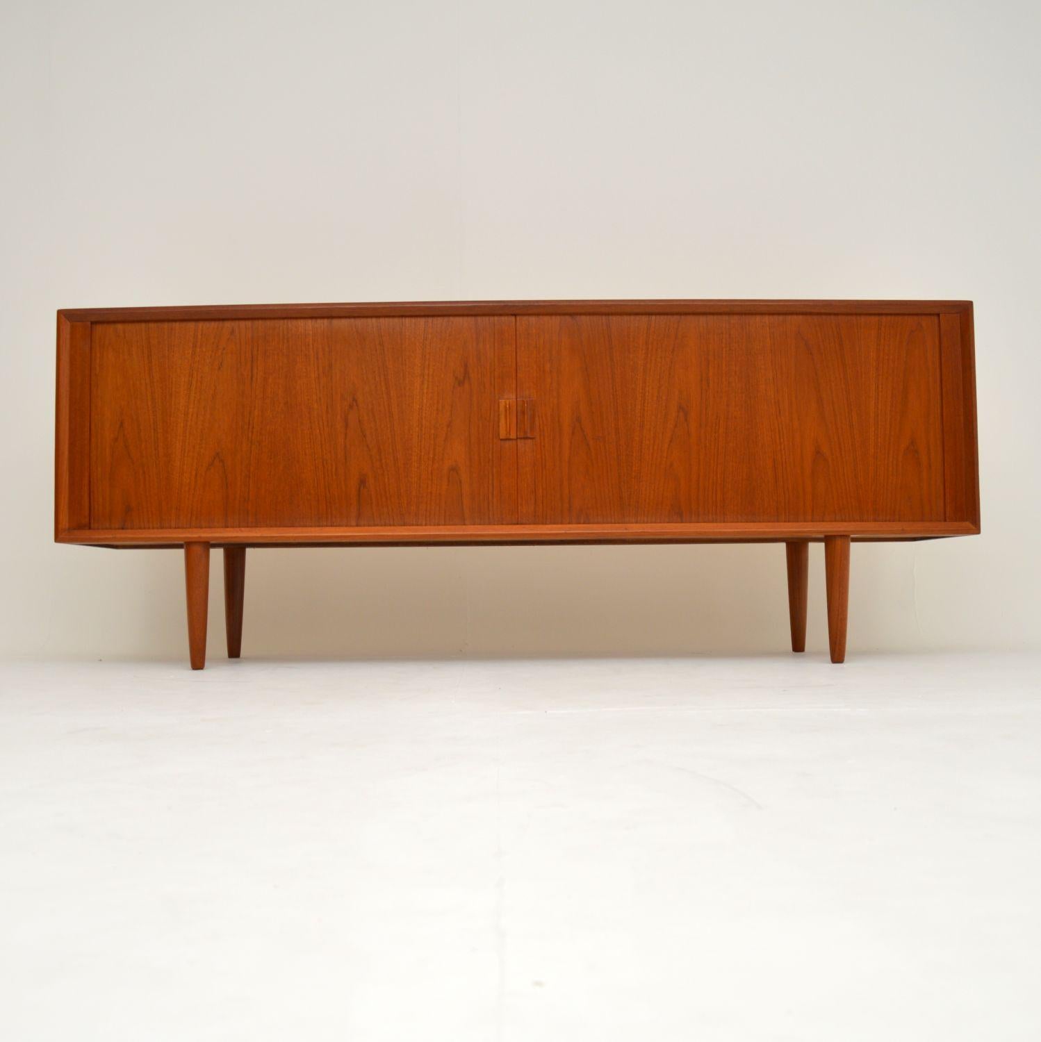 A stunning vintage Danish sideboard in teak. This was designed by Send Aage Larsen Faarup Mobelfabrik, and was made in Denmark in the 1960’s.

The quality is superb, with an amazing tambour door front. The two doors roll back inside the carcass to