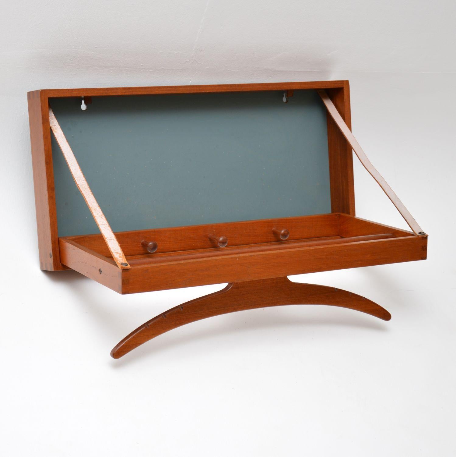 A very cool and rare item, this is a wall mounting clothes valet in teak, it was made in Denmark around the 1960s-1970s. The design is by Adam Hoff and Poul Ostergaard, and its a fabulous design. This easily mounts flush to a wall on two screws, the