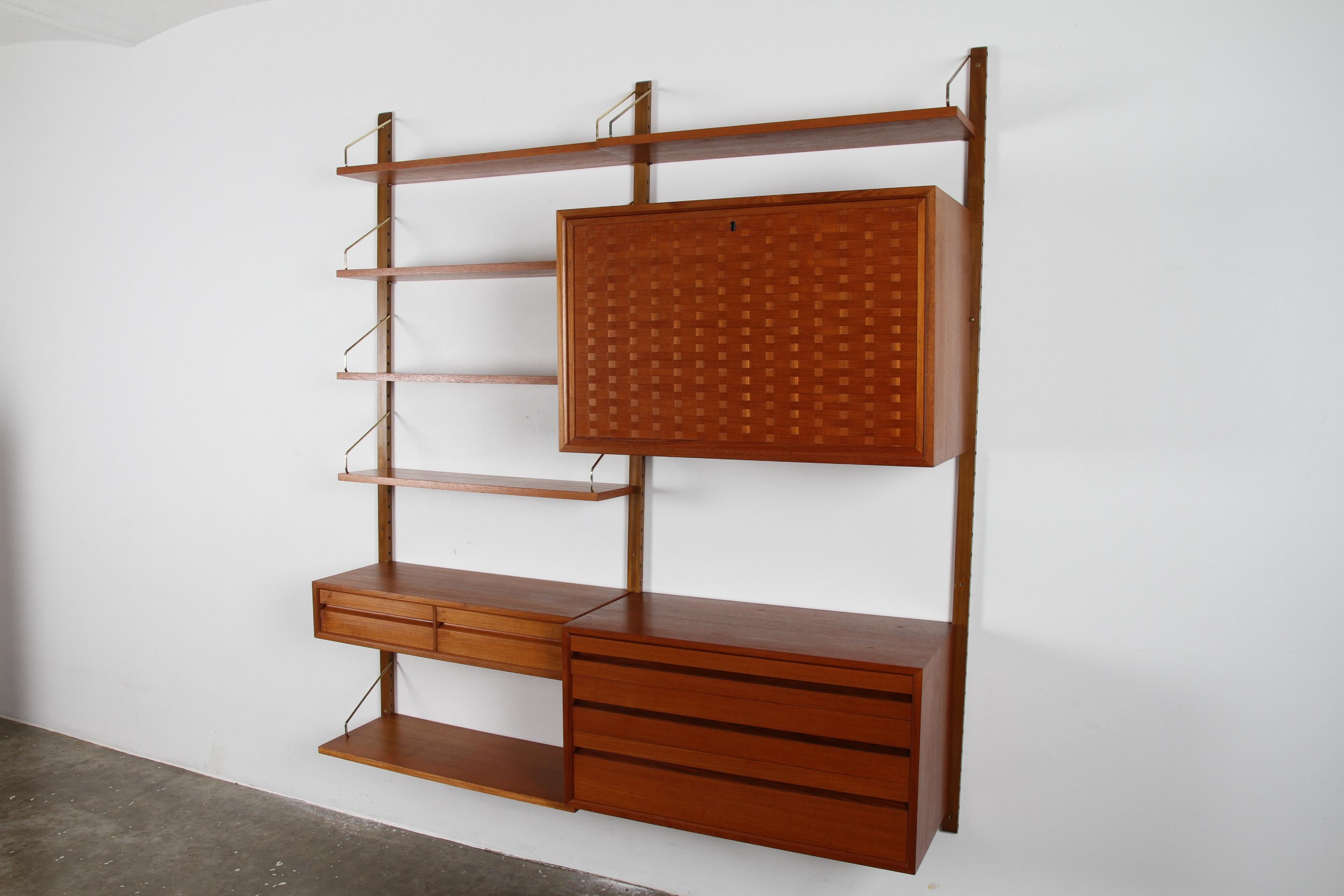 This Mid-Century Modern wall unit consist of 3 uprights, 6 shelves, 1 bar unit, 1 large drawer unit, 1 small drawer unit and 5 rare original bookend sliders.
The bar unit has a stunning woven veneer pattern. And the drawers offers loads of storage