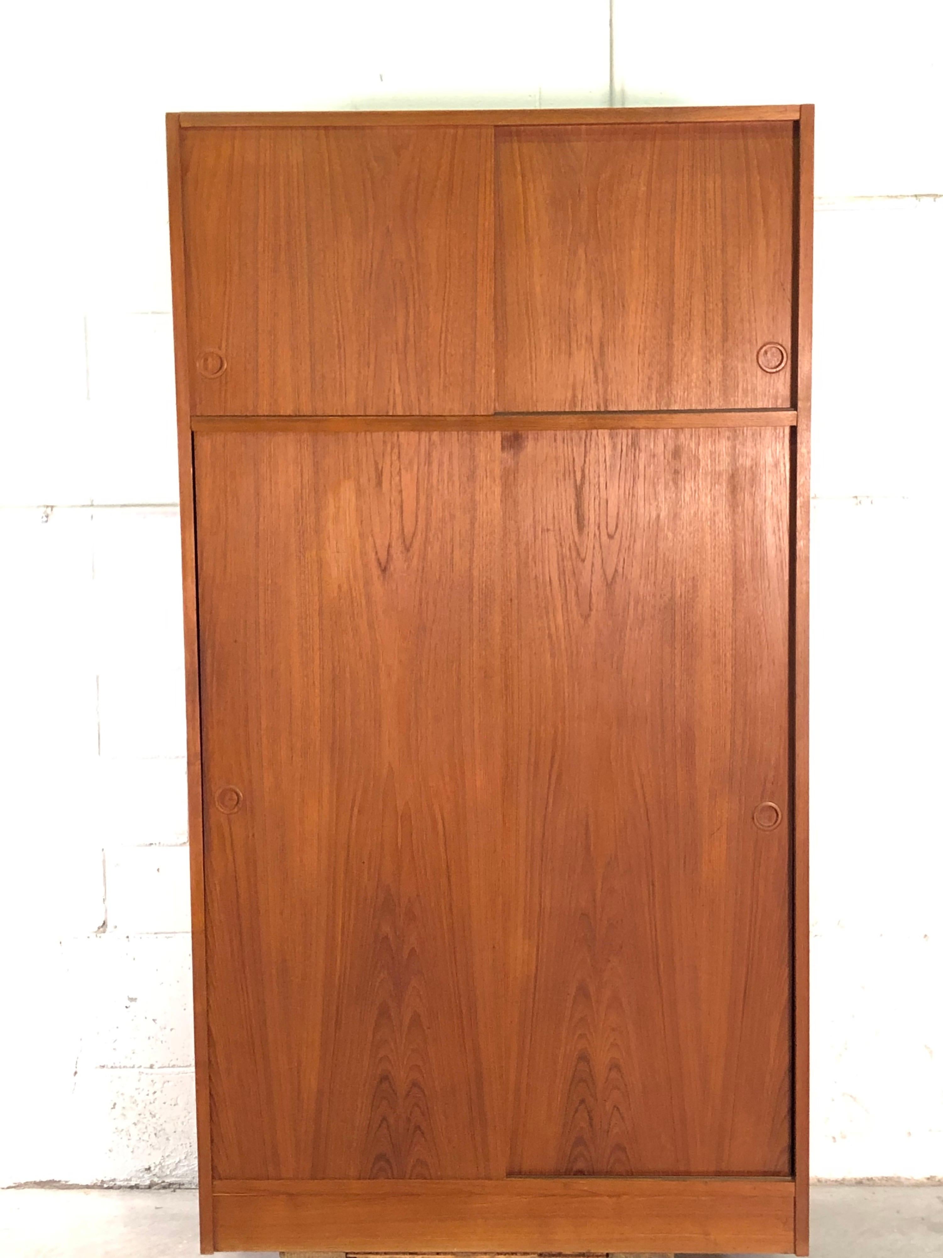Vintage 1960s Danish teak wardrobe armoire designed by Tage Mogensen for the TM Line. The wardrobe offers a lot of storage with sliding doors and circular carved teak inset handles. Open storage on top, shelves that do not adjust on the left side