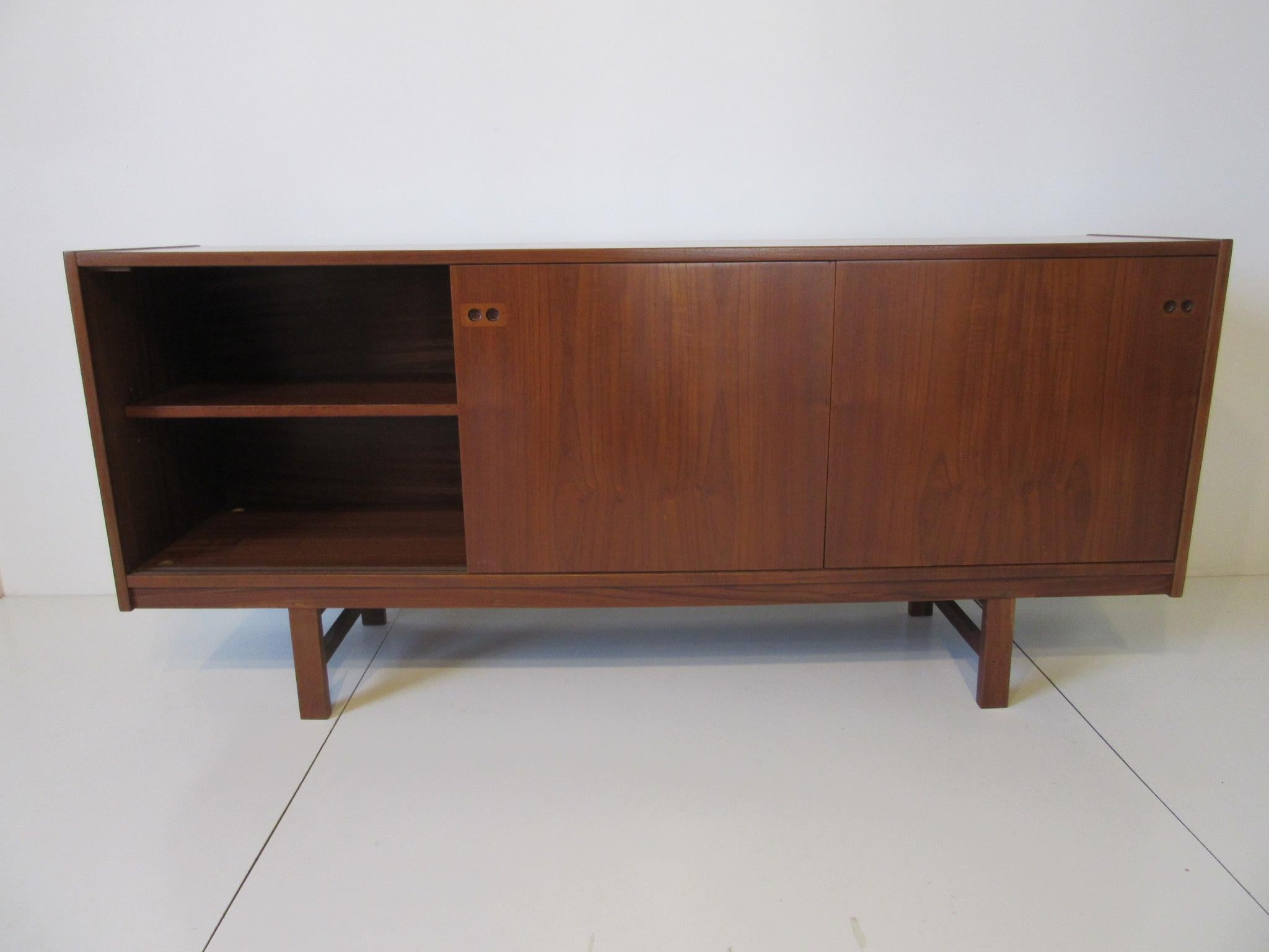 A three sliding door teak wood credenza with one adjustable shelve to each side and the middle section having three slide in shelves. Finger pulls with contrasting wood tone design to the doors and the backside is finished in a flamed grained teak,