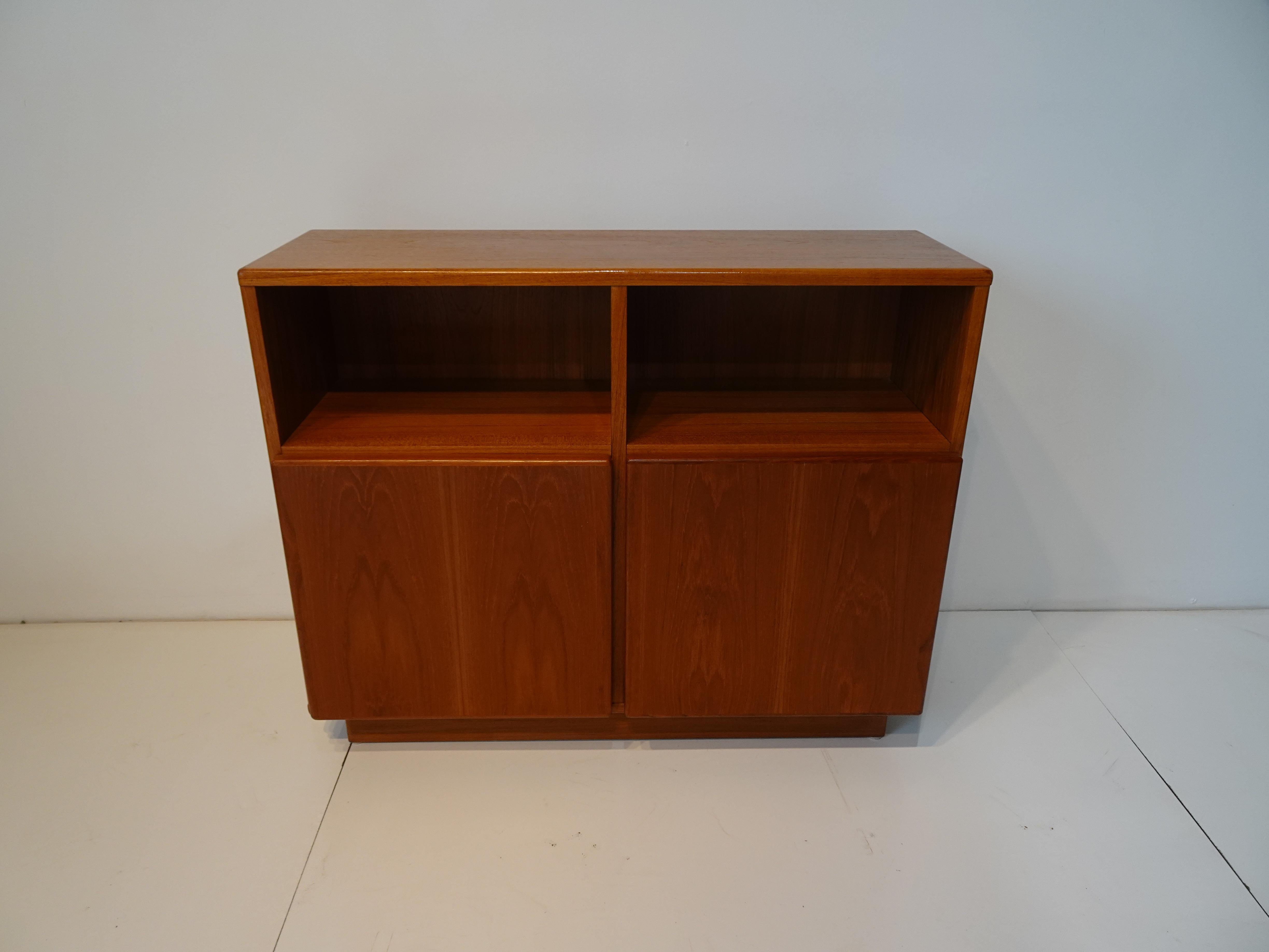 A very slim profiled smaller scale teak wood cabinet with two doors, storage with upper storage bin areas and a finished back . Great for a entrance way , end of hallway or as an entertainment center, the piece is a bit lighter in tone that pictured.