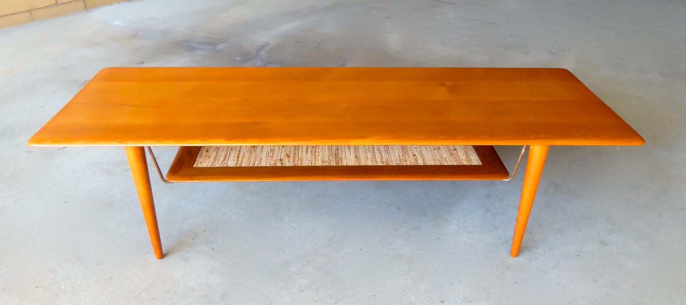 A Danish teakwood coffee table designed by Peter Hvidt and Orla Mølgaard-Nielsen in the 1960s. The coffee table is labeled as manufactured by France & Son and retailed by John Stuart. The lower shelf is supported by metal brackets and hold a shelf
