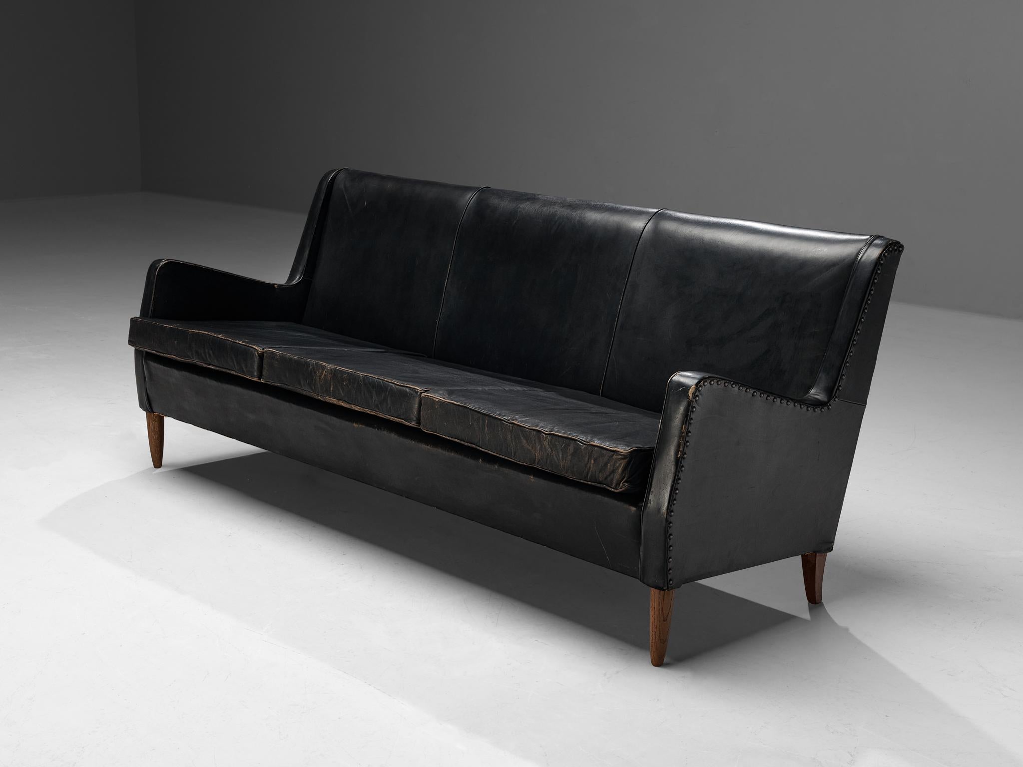 Three-seater sofa, leather, brass, oak, Denmark 1950s. 

Elegant three-seat sofa in original leather and decorated with brass nails. This sofa is designed in the style of Frits Henningsen and manufacturer Rud Rasmussen. The tapered legs are made of