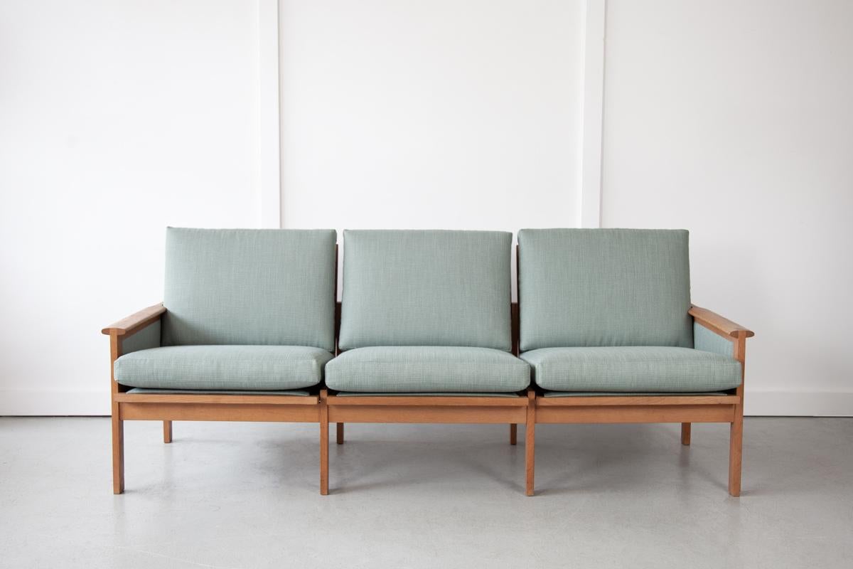 The handsome 'Capella' sofa by Illum Wikkelsø for Niels Eilersen, with an elegant solid oak frame that displays a relaxed stance and slatted back. The sofa has been fully restored with new webbing, new foam box cushions with remove-able zip covers