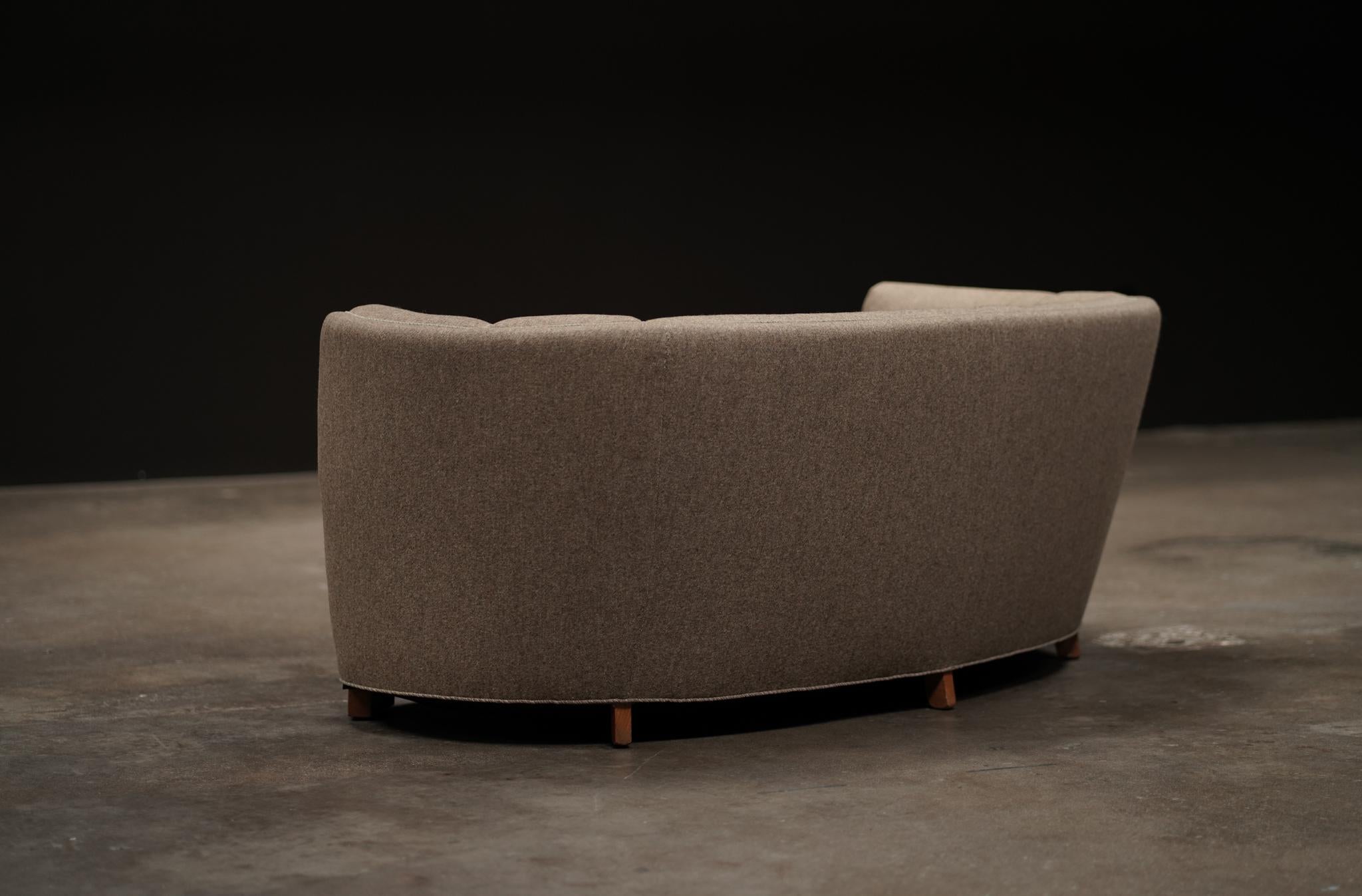 This Danish three-seater sofa features an elegant curved back and is upholstered in its original striped linen, lending a sense of understated charm. Resting on simple deco style wood feet, it offers both sculptural presence and timeless comfort. I