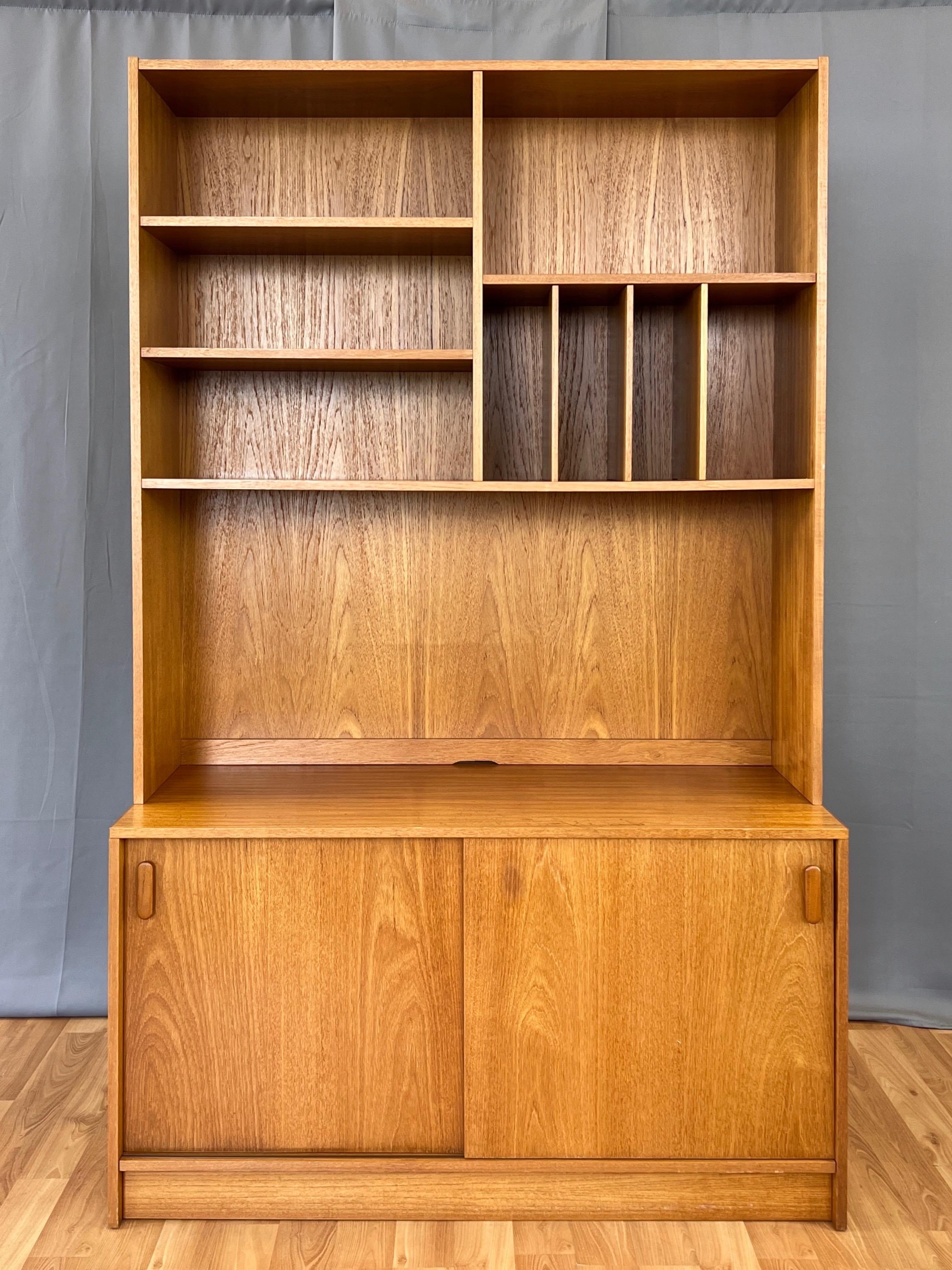 A 1970s Poul Hundevad-style tall Danish modern teak hutch with bookcase and cabinet by UP Møbelfabrik.

Upper portion with a variety of 11.5-inch-deep spaces perfect for books, collectibles, curios, and the like. Largest bottom space features a