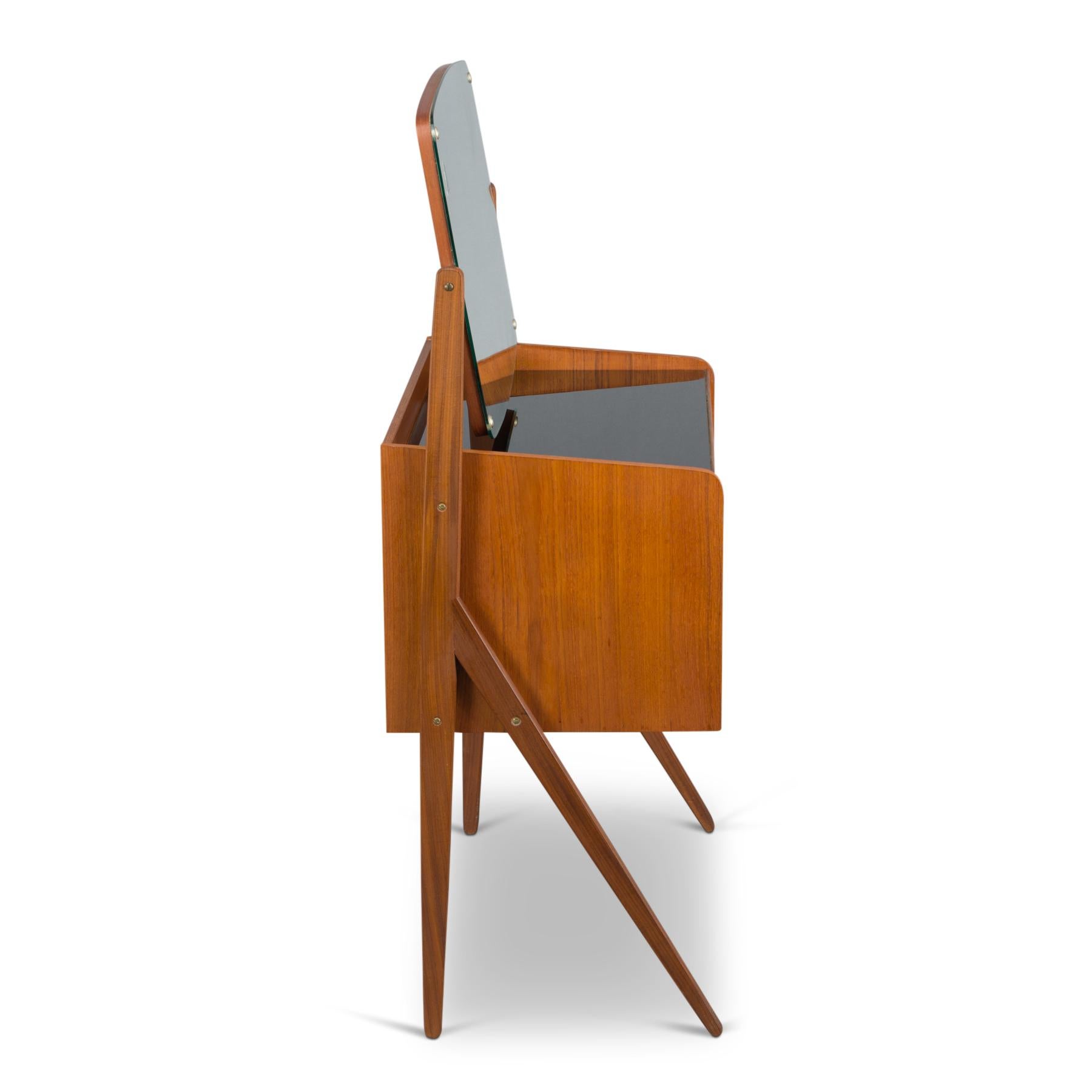 Danish Mid-Century Modern design vanity that will love you. This Danish beauty is made in teak veneer. The mirror of this vanity is oval shaped and suspended from the elegant legs of the vanity. The drawers are of different sizes and ideal to hold