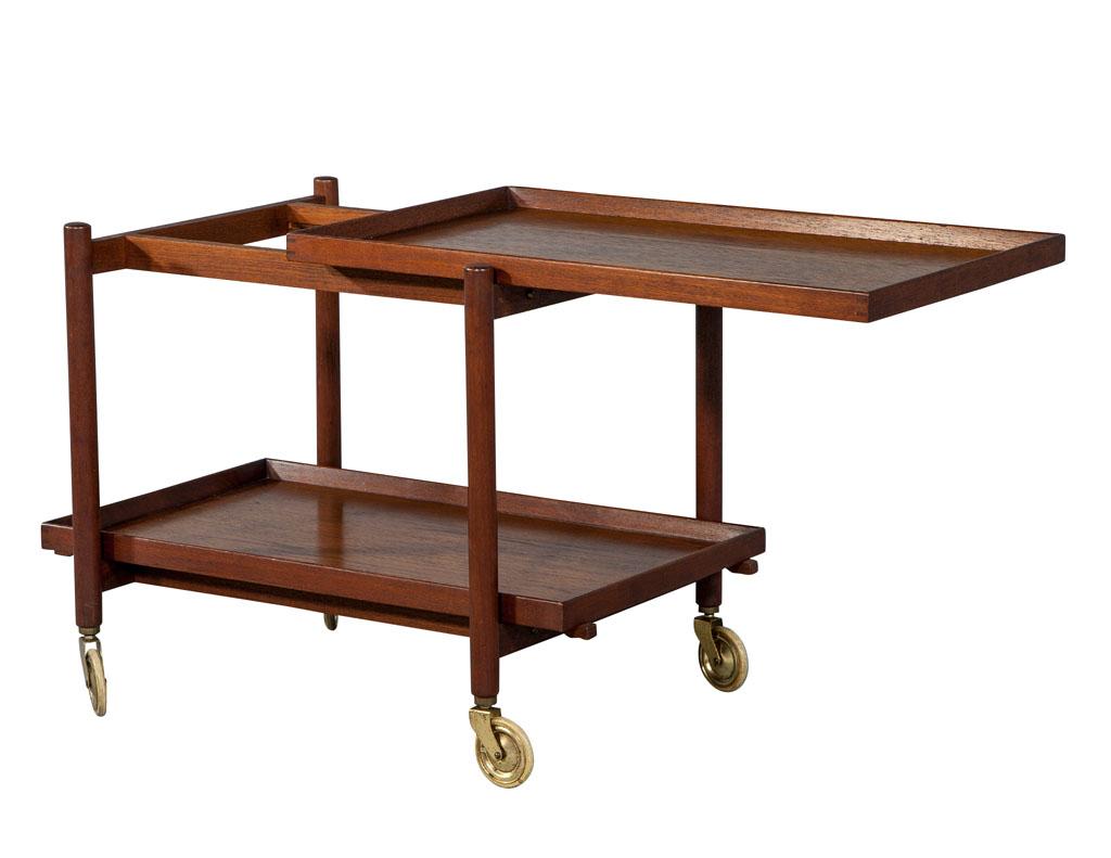 Danish vintage midcentury teak bar cart tea caddy trolley. This vintage original trolley hails from Denmark and is truly representative of the simplicity that is Danish design. This trolley has its original brass wheels, a floating top shelf and a
