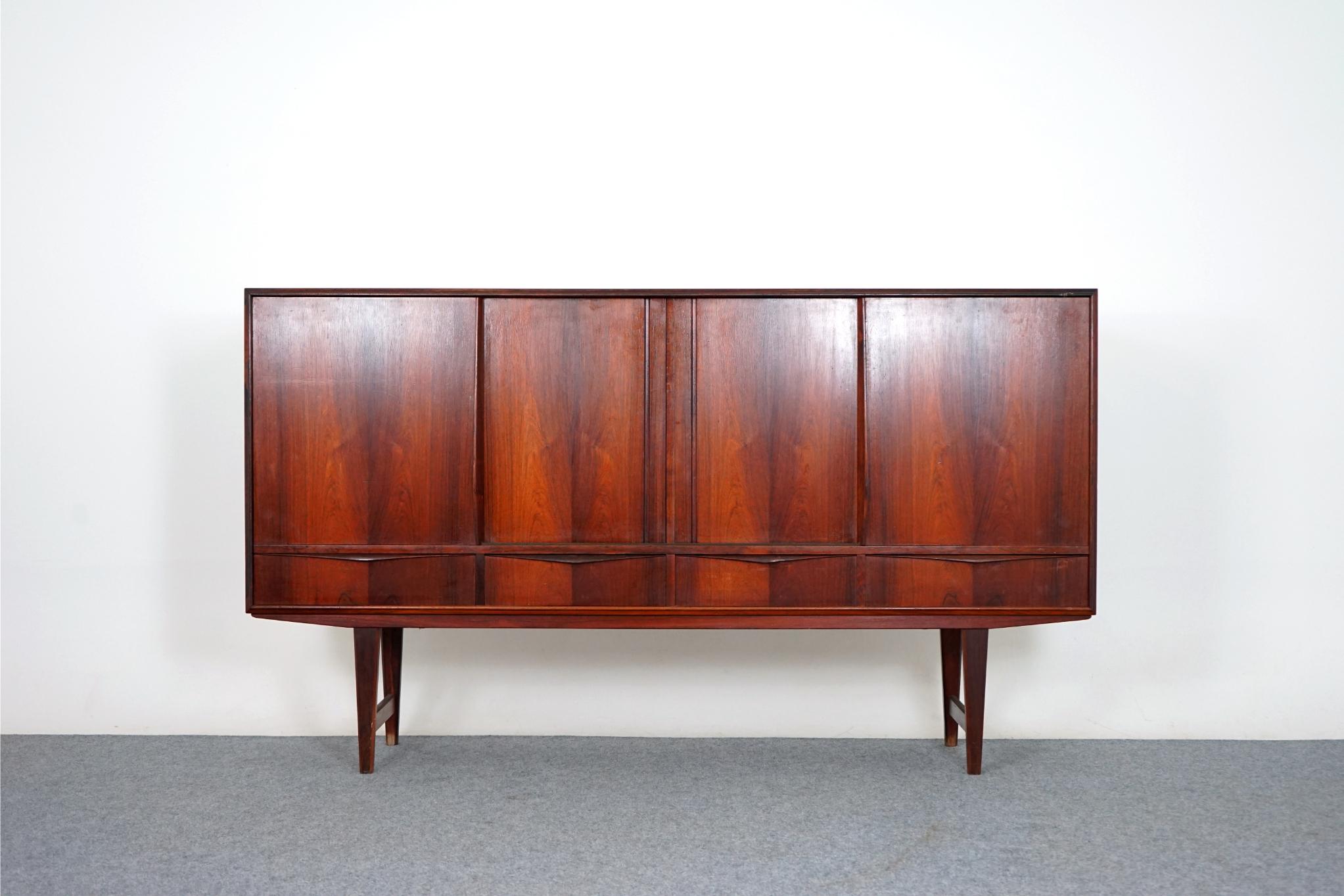 Rosewood Danish sideboard, circa 1960's. Clean, simple lined design highlights the exceptional book-matched veneer throughout. A combination of sliding doors and exterior drawers offers ample storage options. Interior bays are outfitted with