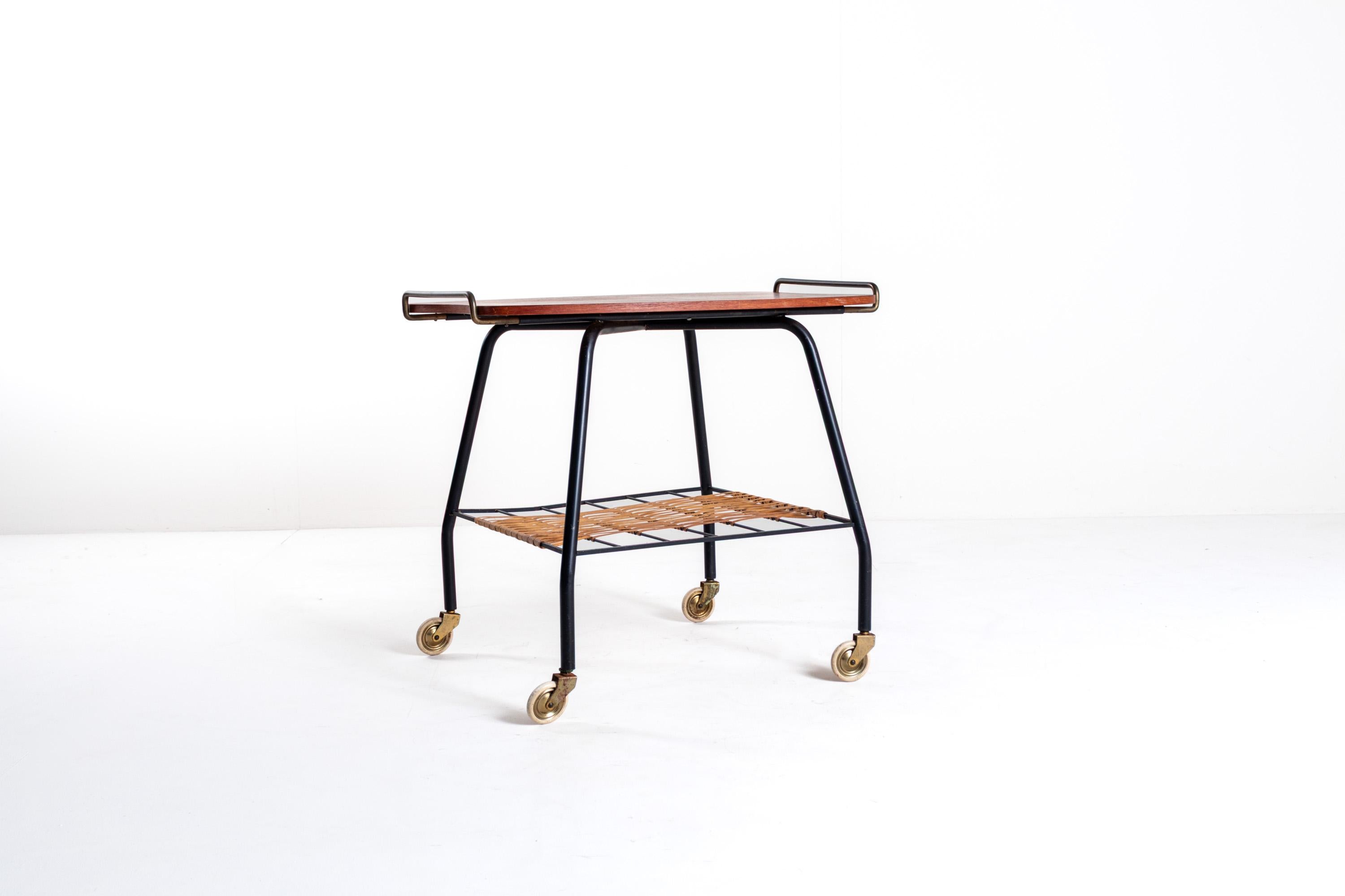 This Danish vintage serving cart and/or tea trolley from the 1950s is a stylish piece with an elegant design. The top is made of teak wood, complemented by brass handles that add a refined touch. The lower section features a woven rattan magazine